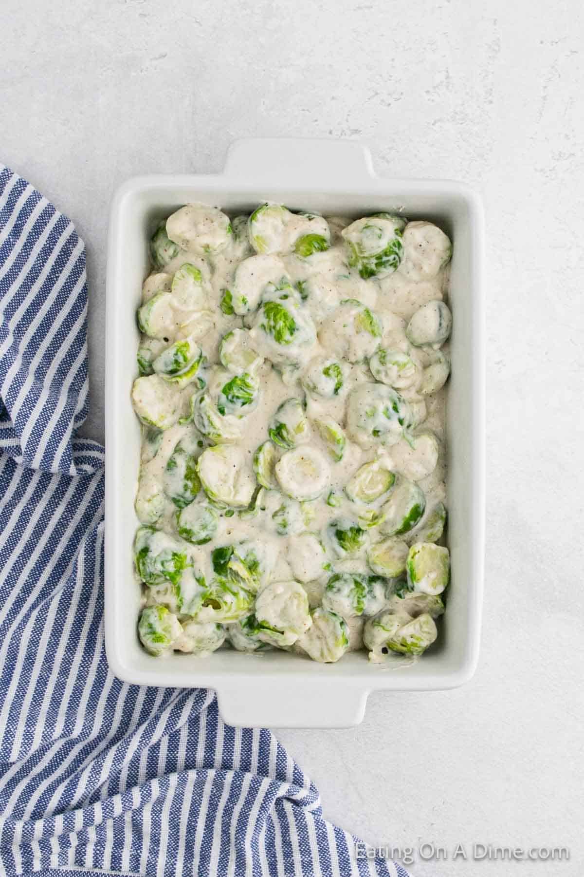 Casserole dish filled with creamy Brussel sprouts au gratin. A blue and white striped towel is partially visible on the side, adding a cozy touch to this delightful recipe.