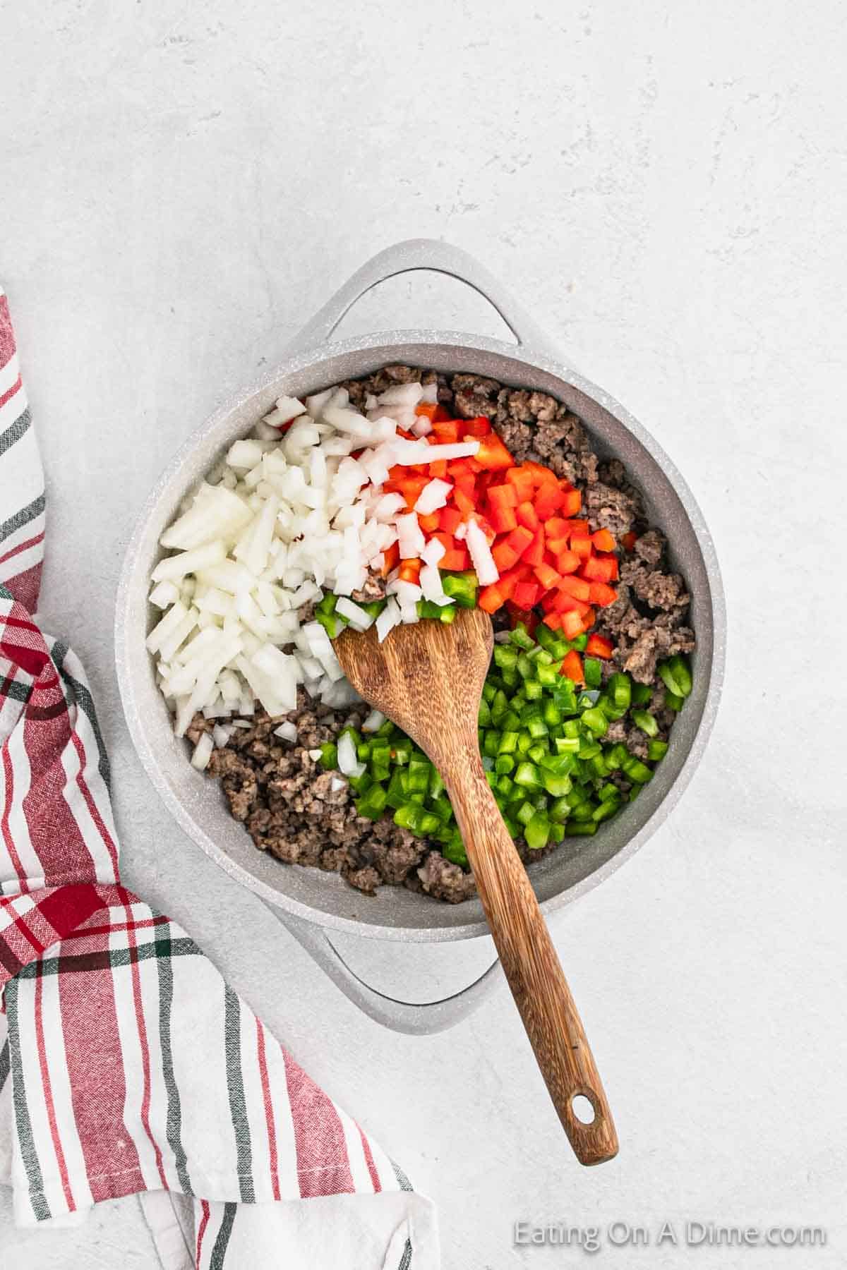 Cooked sausage, diced onions, red bell peppers and green bell peppers in a skillet with a wooden spoon