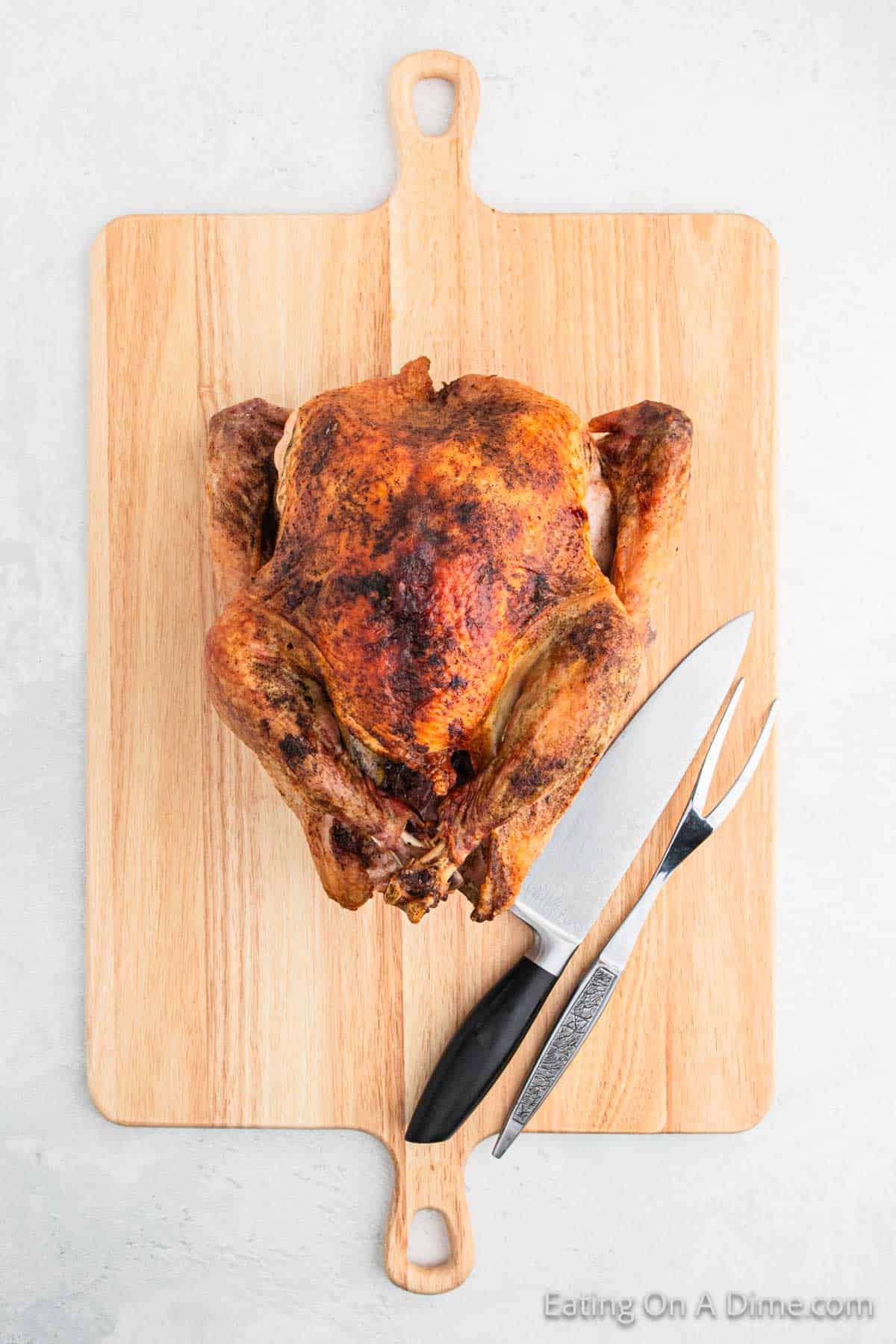 A whole roasted chicken, golden brown, sits on a wooden cutting board. Beside it, a carving knife and fork invite you to master the art of how to carve with precision.