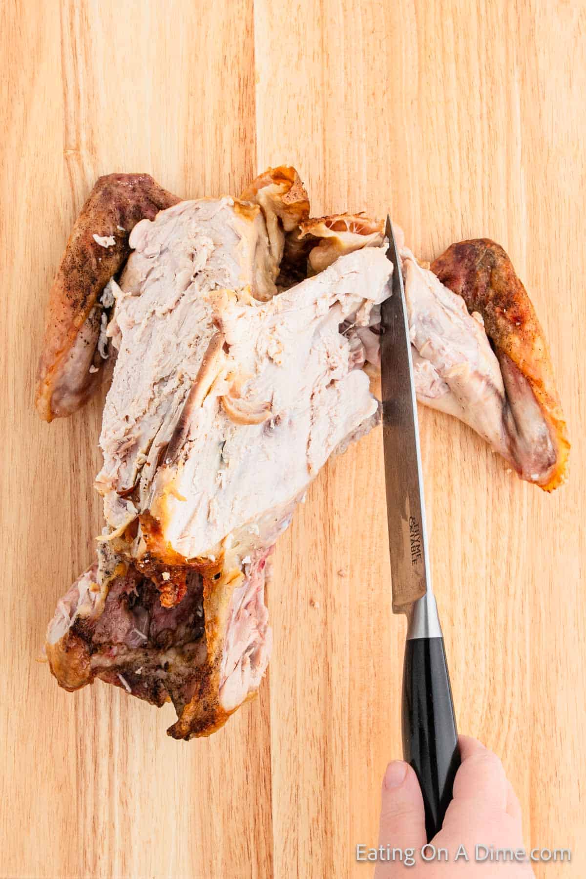 A person expertly carving a cooked chicken on a wooden surface, demonstrating skills that could easily transition to turkey carving.