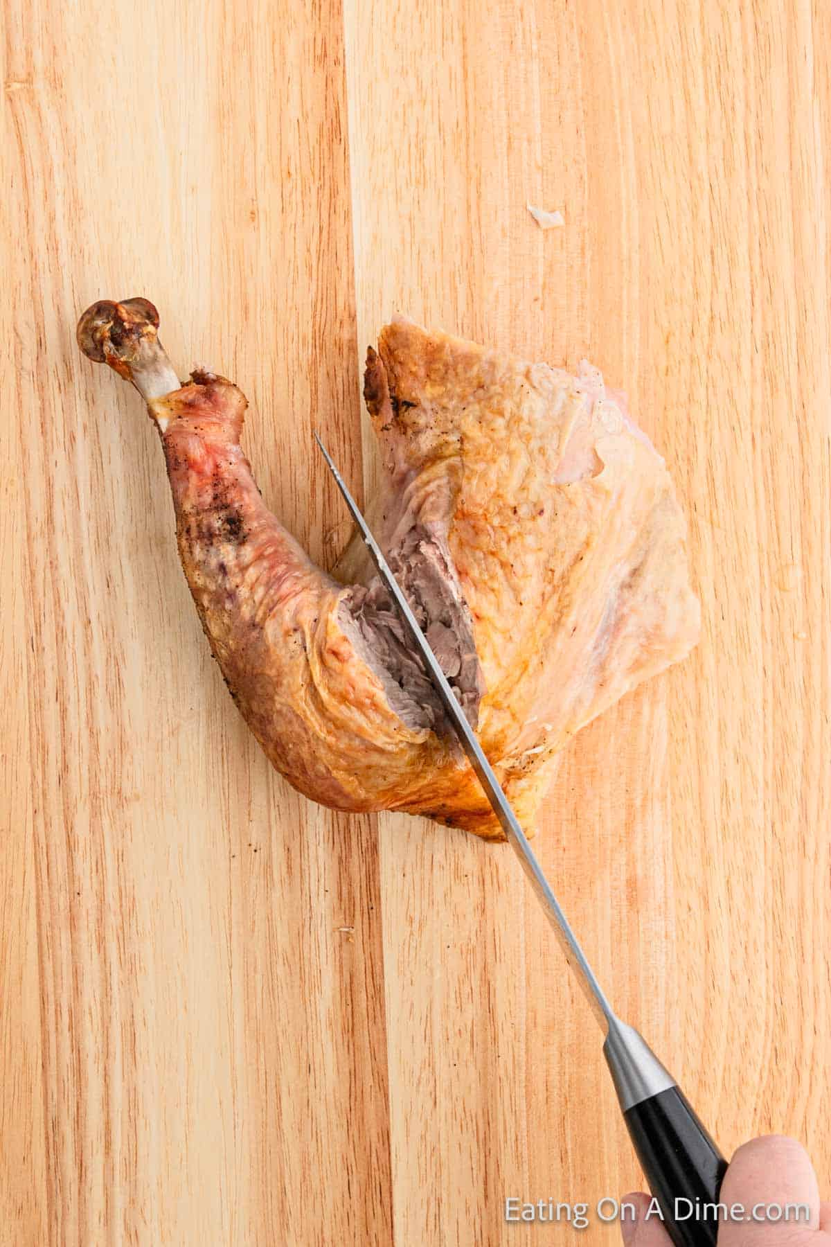 A person skillfully demonstrating how to carve a turkey, expertly slicing a cooked turkey leg on a wooden cutting board with a sharp knife. The turkey leg boasts crispy, golden-brown skin.