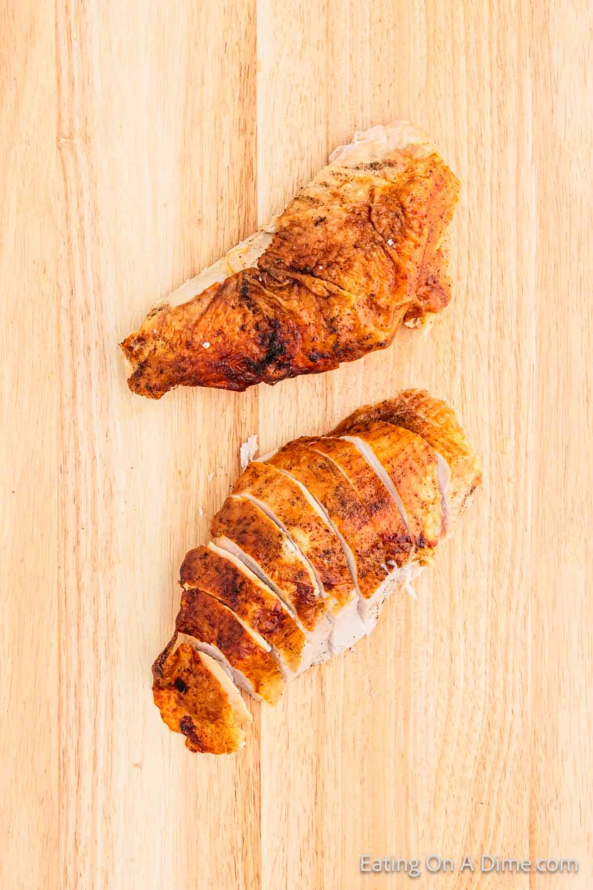 Two pieces of roasted chicken breast rest on a wooden cutting board. One piece is sliced, revealing its juicy interior, while the other remains whole with crispy golden skin. This mouthwatering display is reminiscent of expert turkey carving tips for achieving perfect results every time.