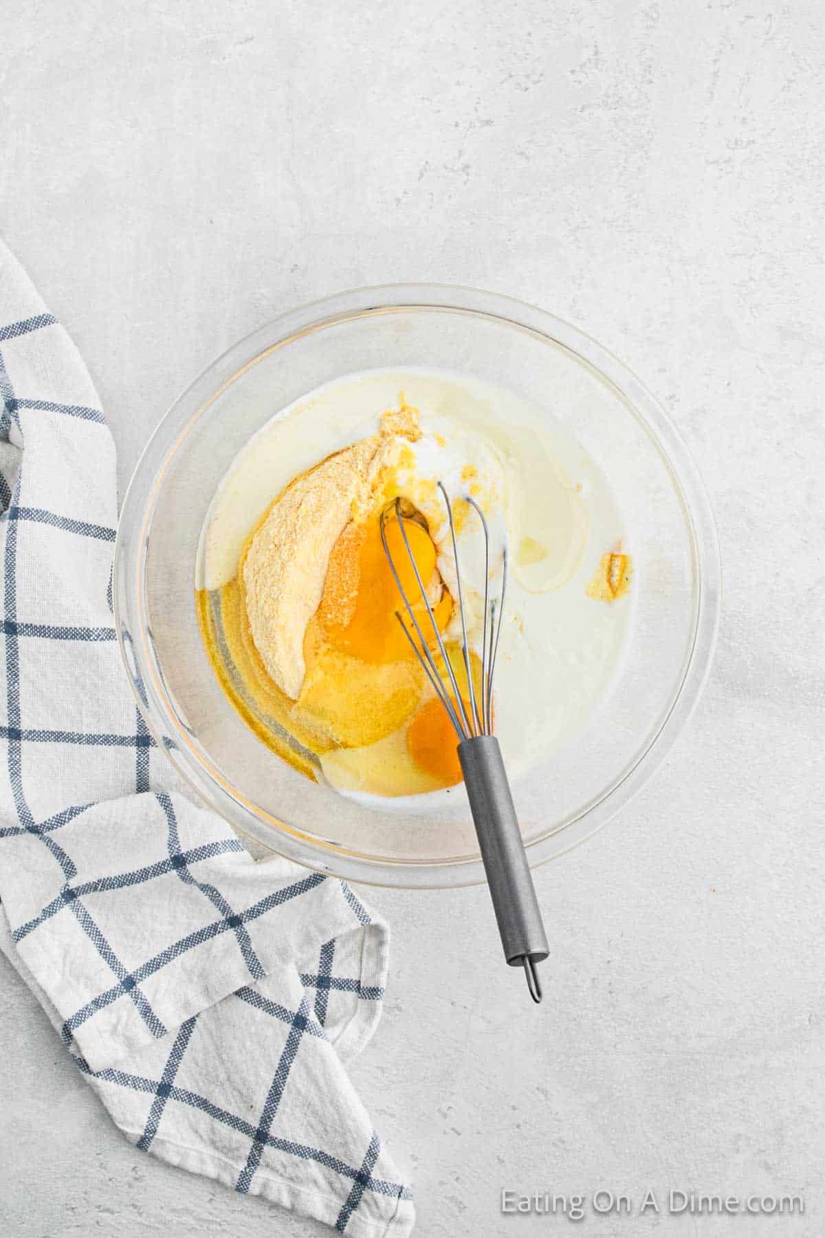 Mixing Cornmeal, oil, buttermilk, and eggs together in a bowl with a whisk