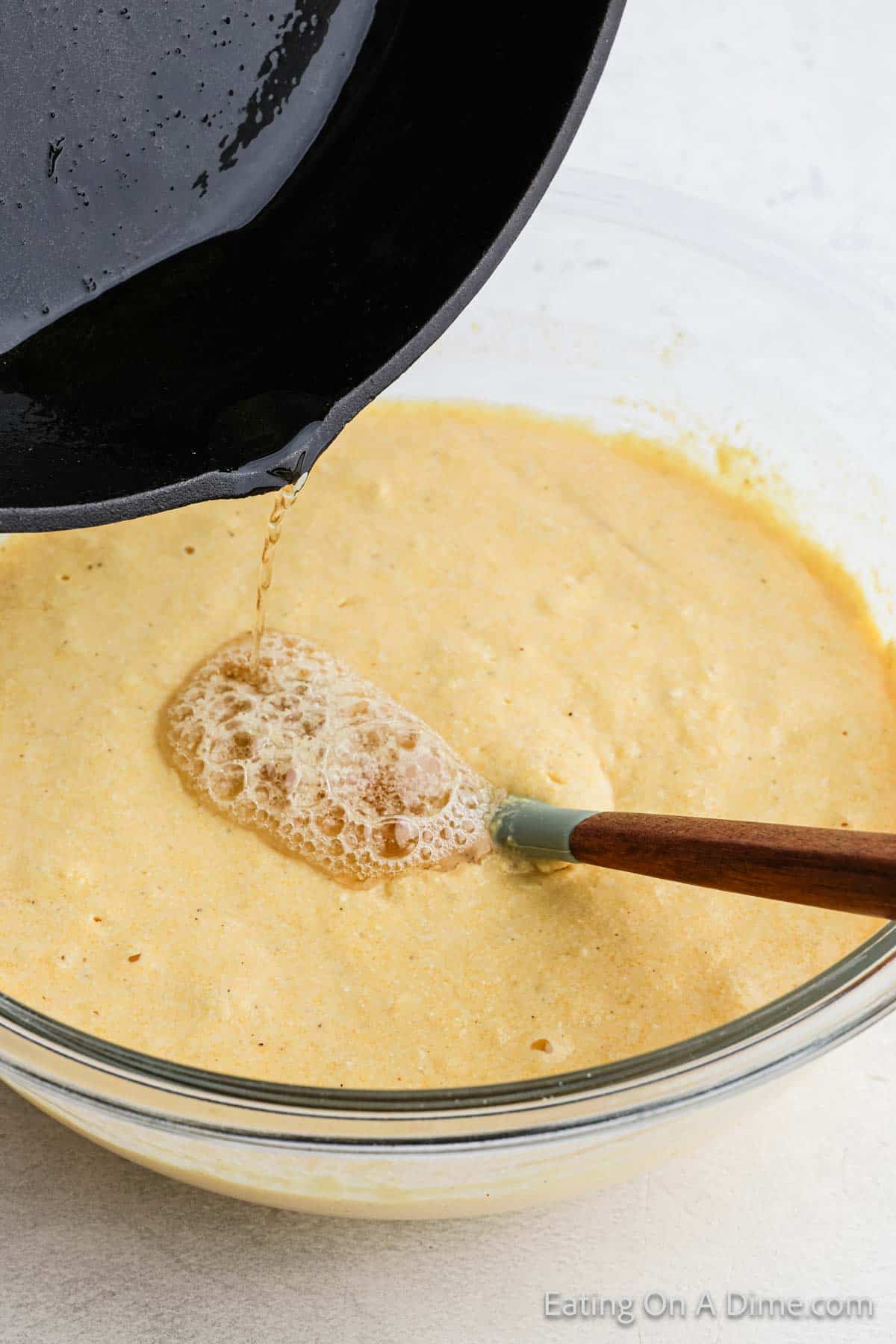 Cornbread batter in a clear bowl with the leftover grease being mixed in the batter