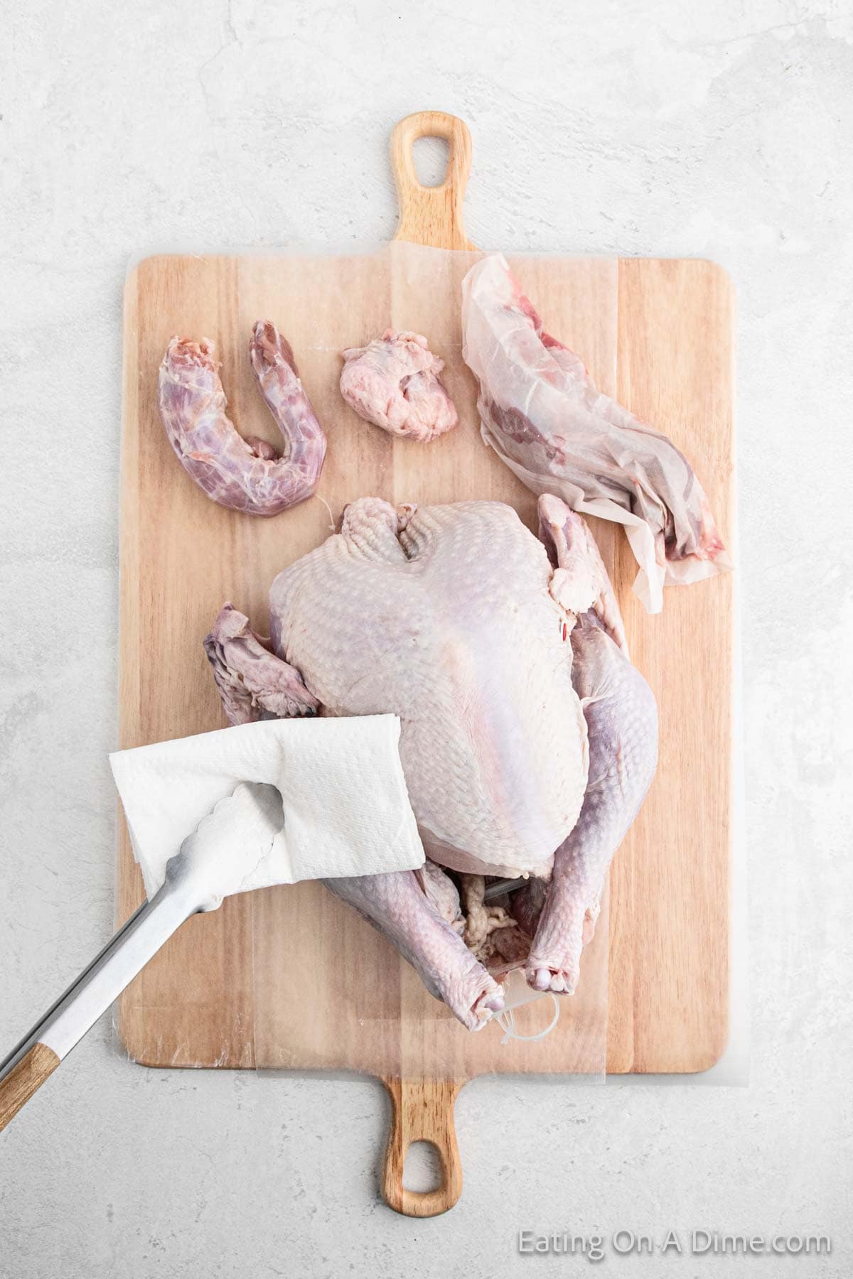 Whole turkey on a cutting board being dried with a paper towel and the giblets removed from the turkey