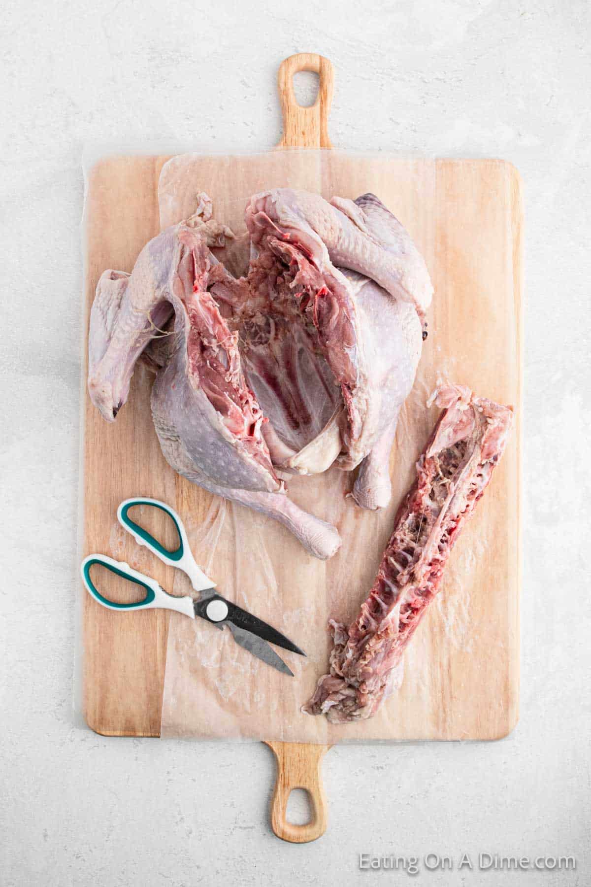 Backbone of the turkey being removed from the whole turkey on the cutting board with kitchen shears