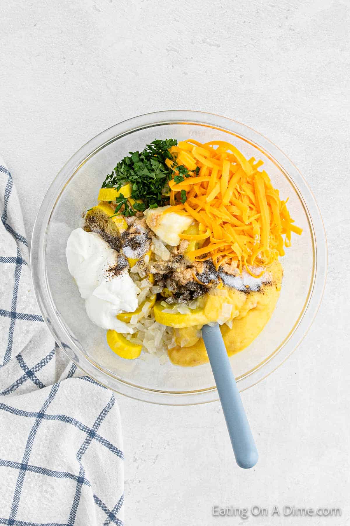 Combining slice squash, shredded cheese, sour cream and seasoning in a bowl with a spatula