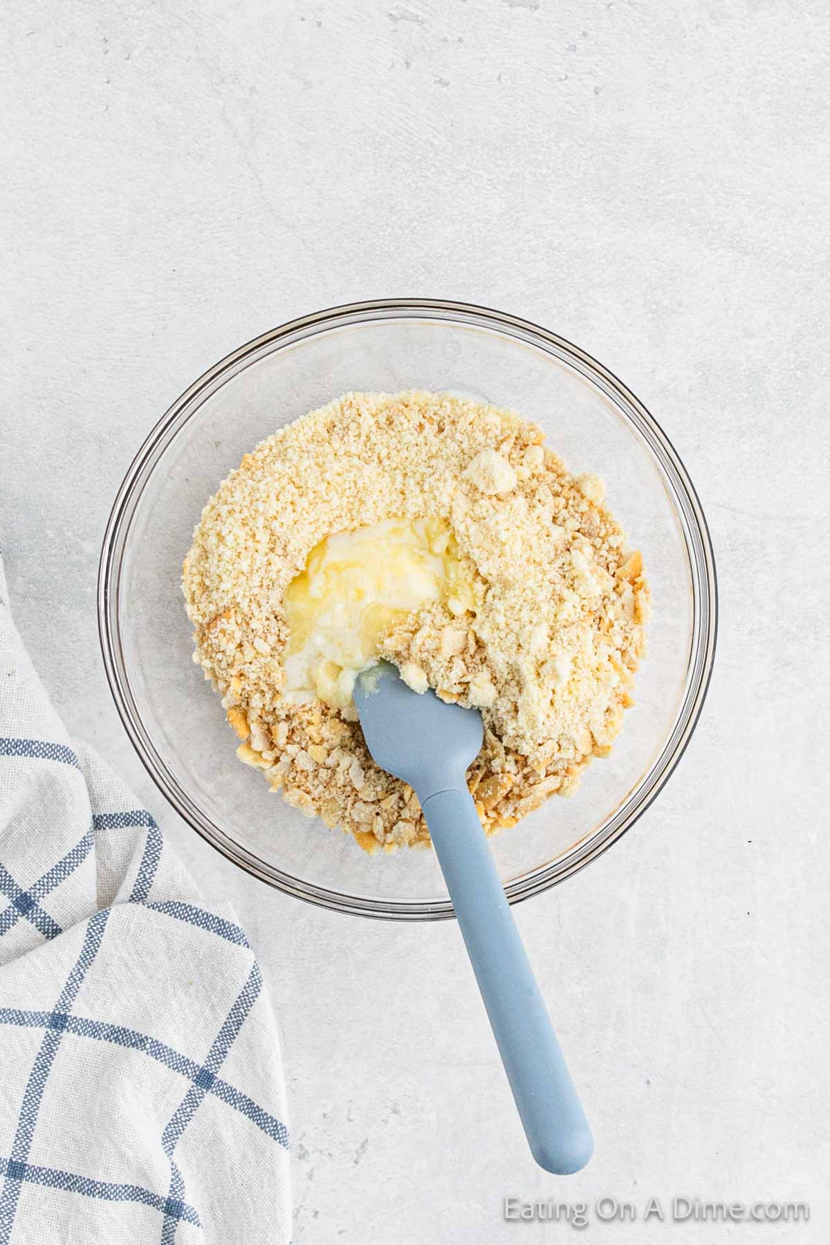 Combining crushed crackers, melted butter and parmesan cheese in a bowl