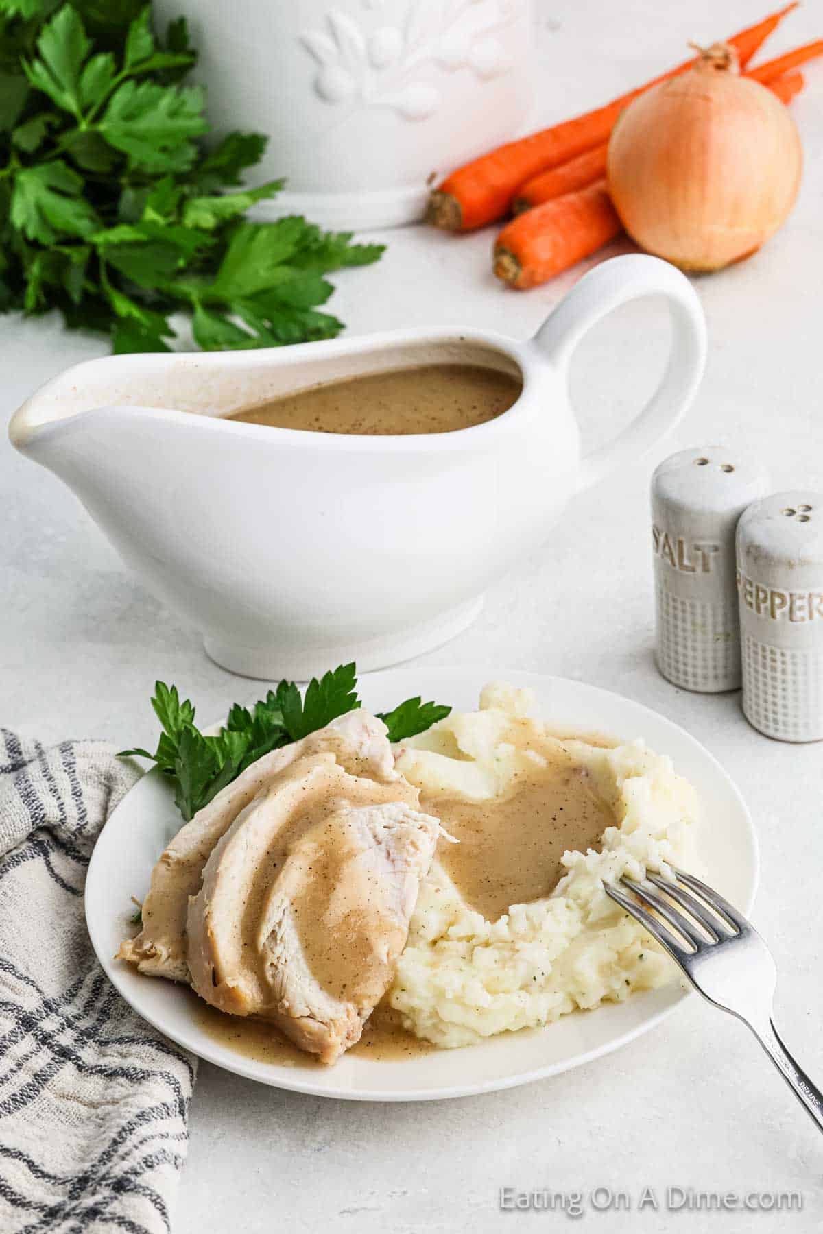 Brown gravy poured over sliced turkey and mashed potatoes with gravy in a large white turkey serving dish 