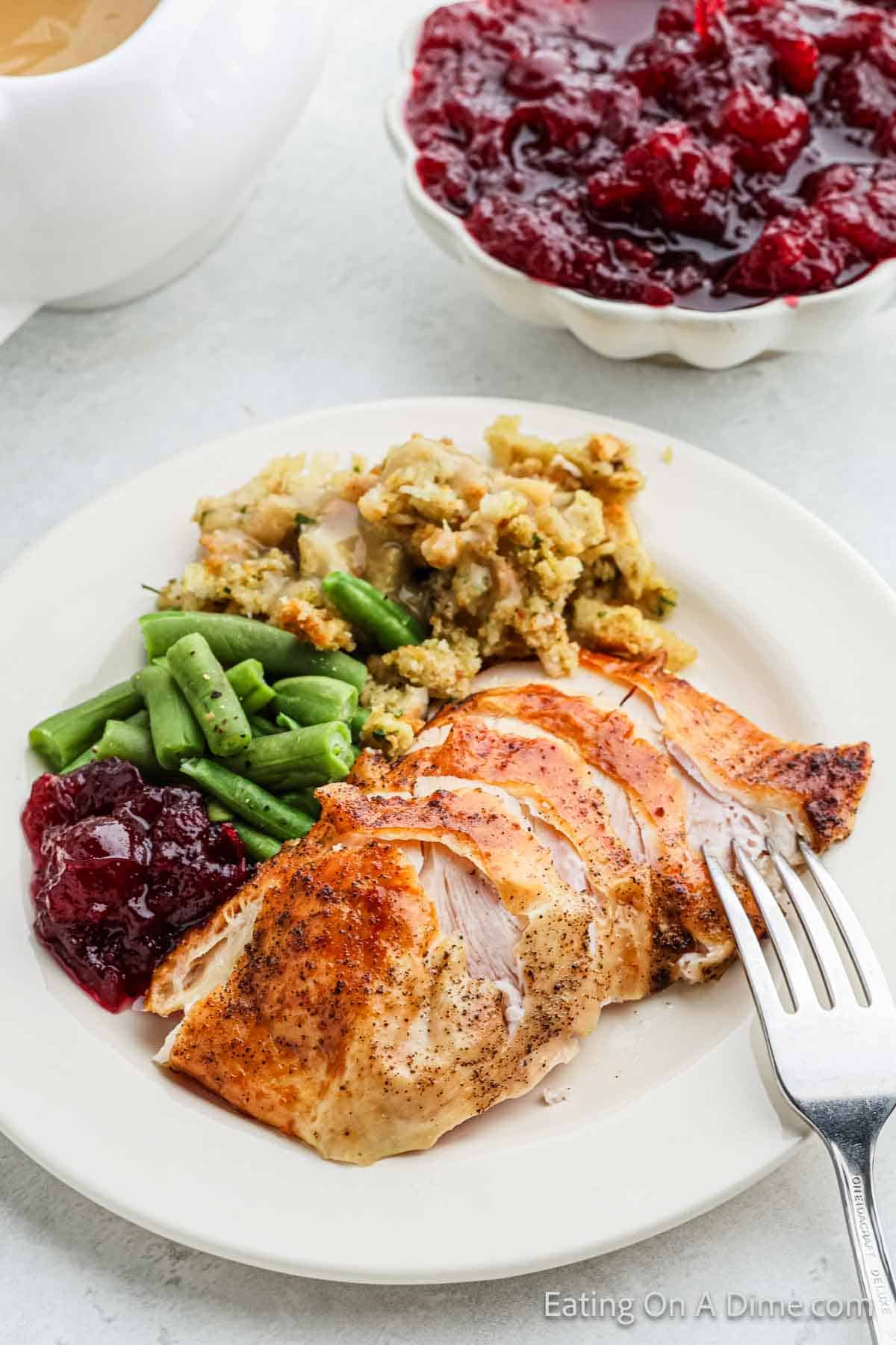 Turkey Breast on a plate with a side of stuffing, green beans and cranberry sauce