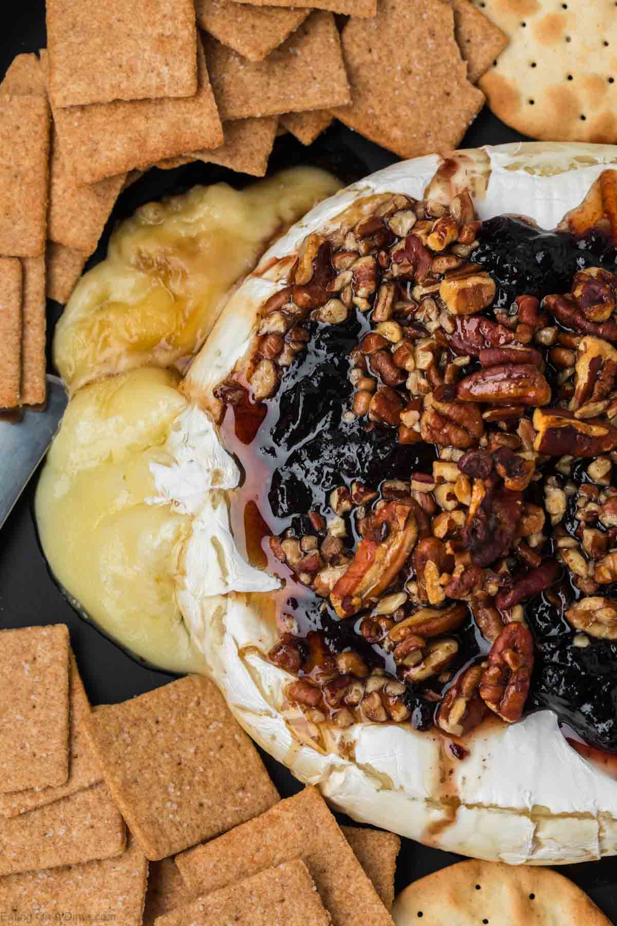 Baked Brie topped with jam and chopped pecans with a side of crackers on a platter