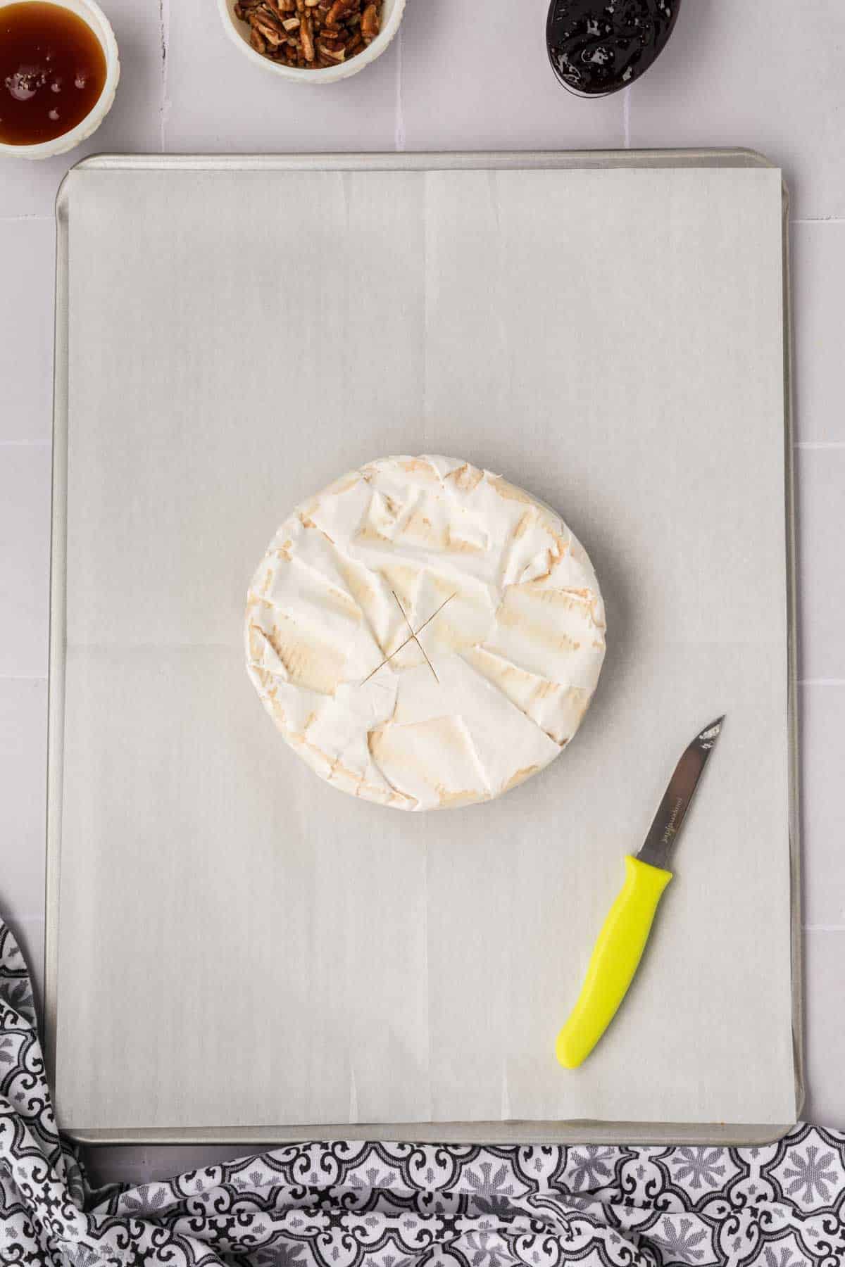 Wheel of Brie on a baking sheet lined with parchment paper that has been sliced with a knife