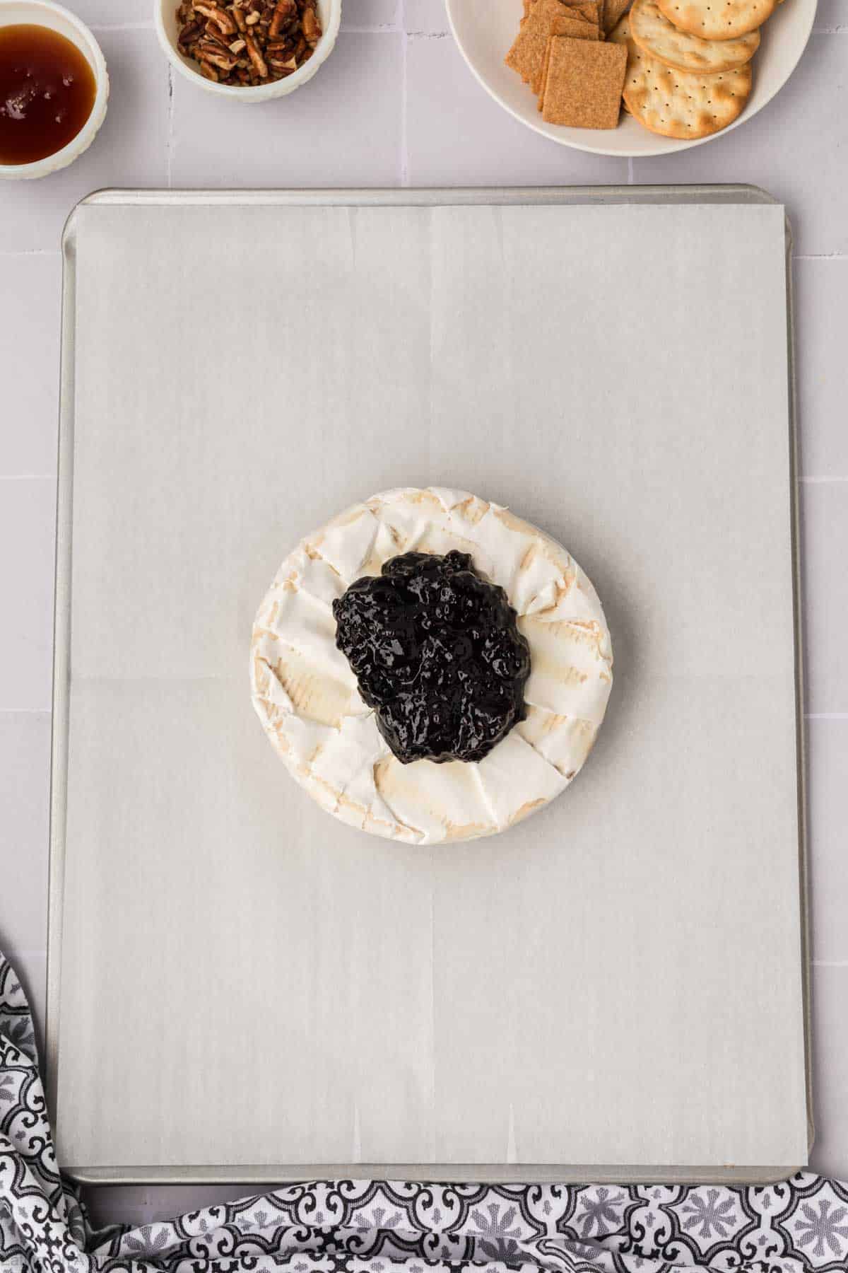 Wheel of Brie topped with jelly on a baking sheet lined with parchment paper