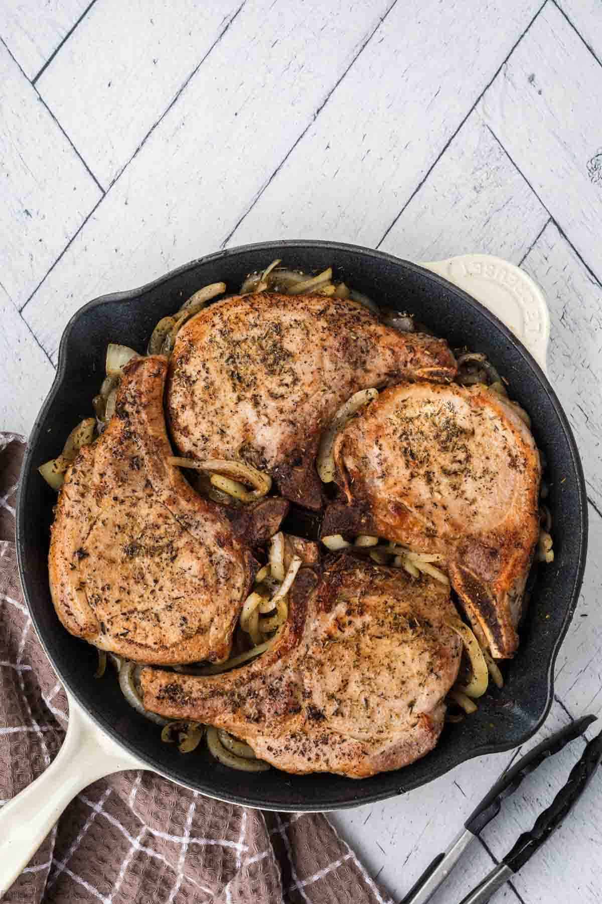 Cooked pork chops in a skillet over cooked onions