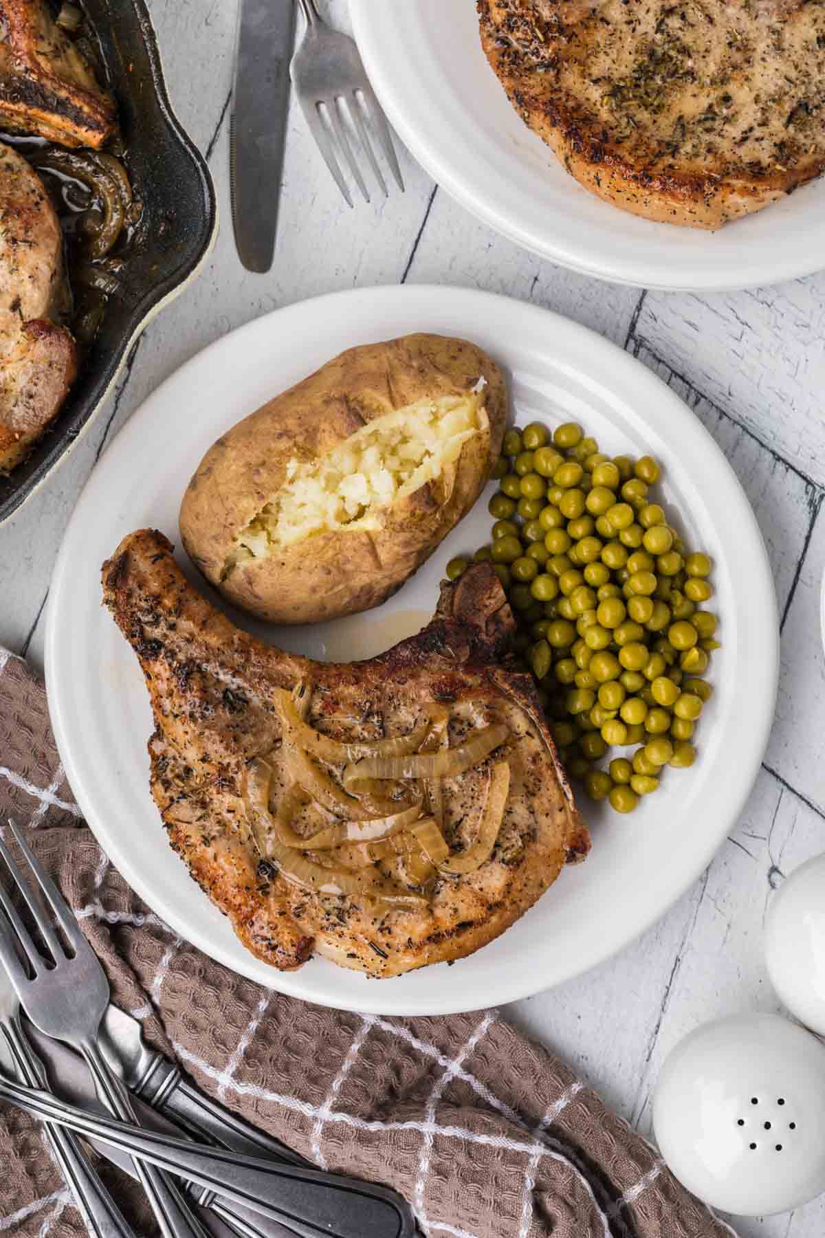 Cooked pork chops on a plate with peas and baked potato on a plate