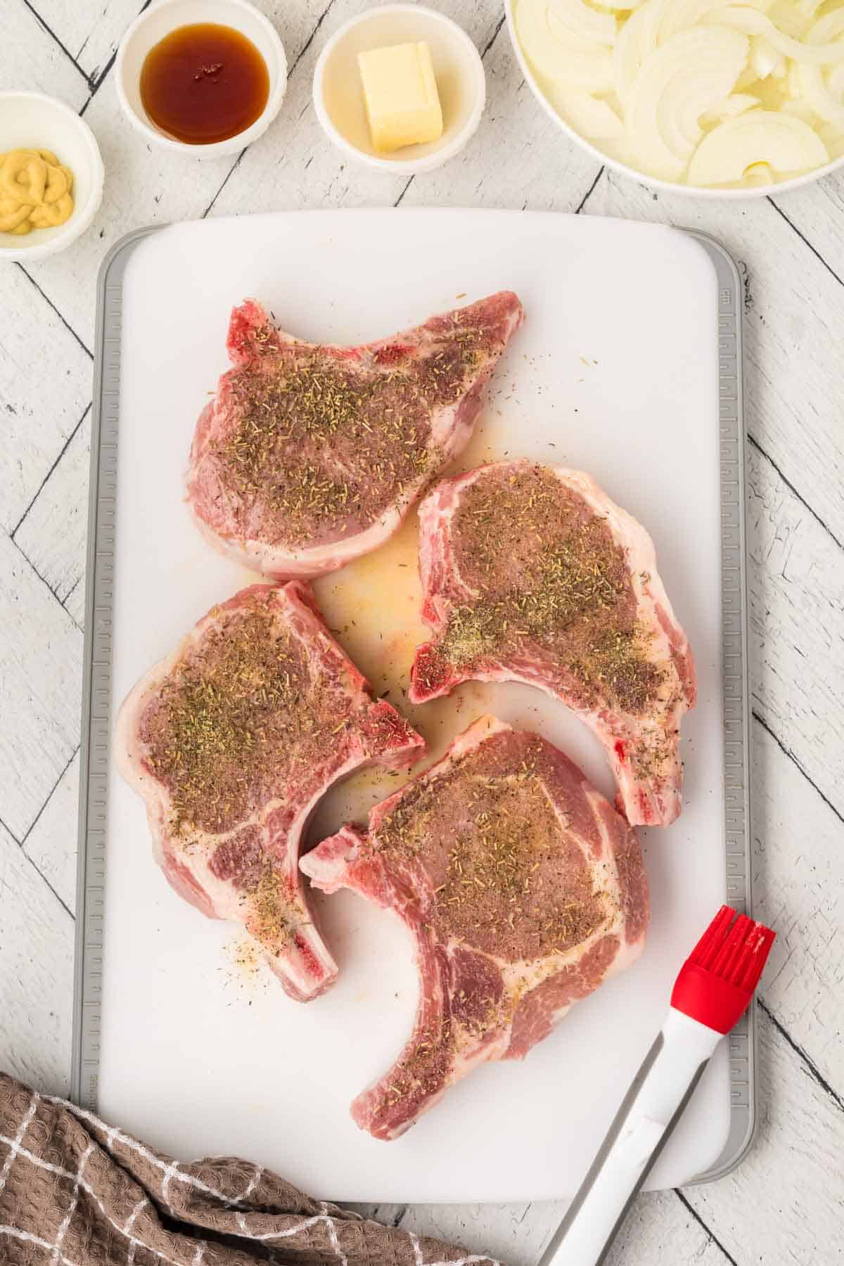 Adding the seasoning mixture over the bone in pork chops on a cutting board