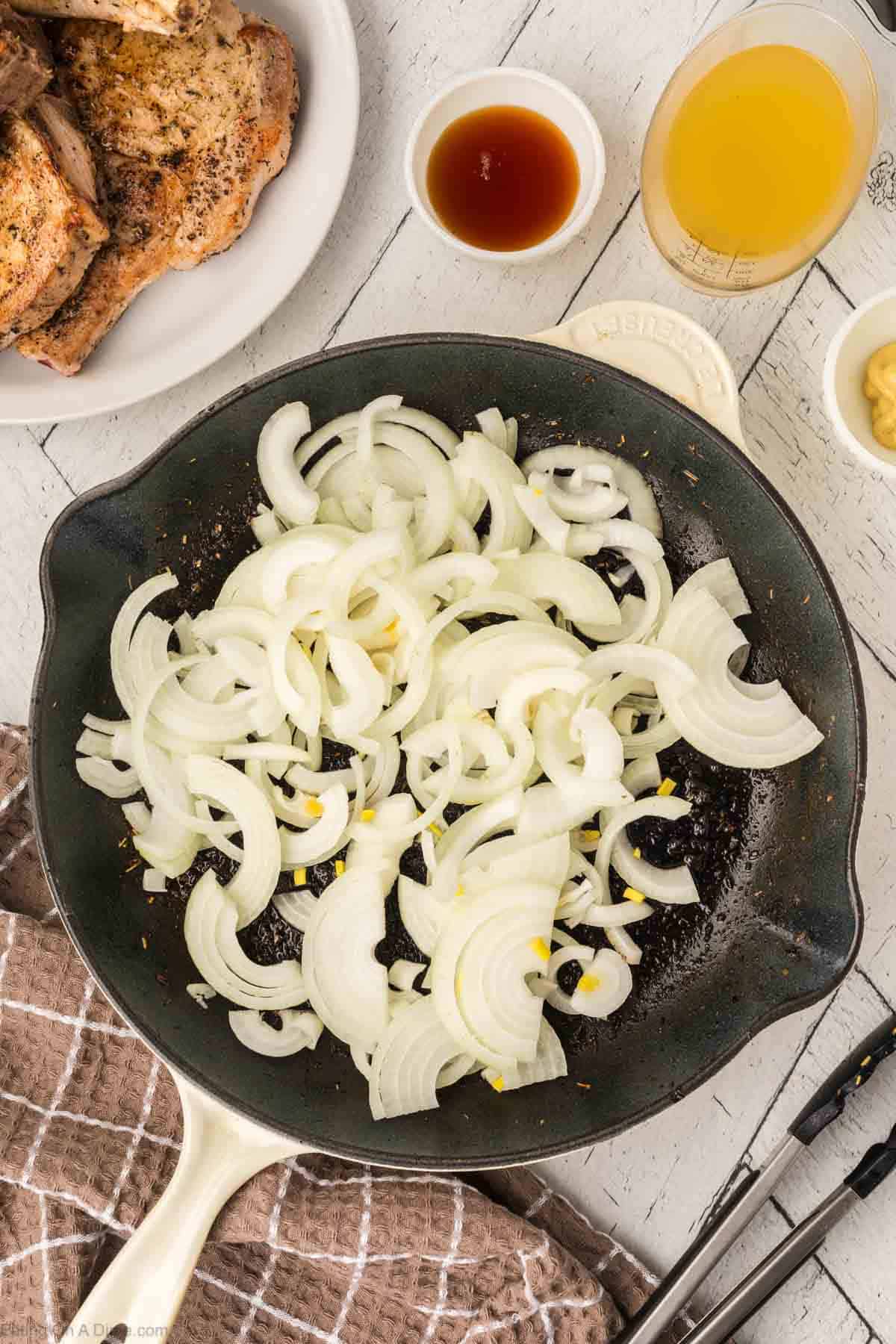 Chopped onions in a skillet with a cooked pork chops on a plate