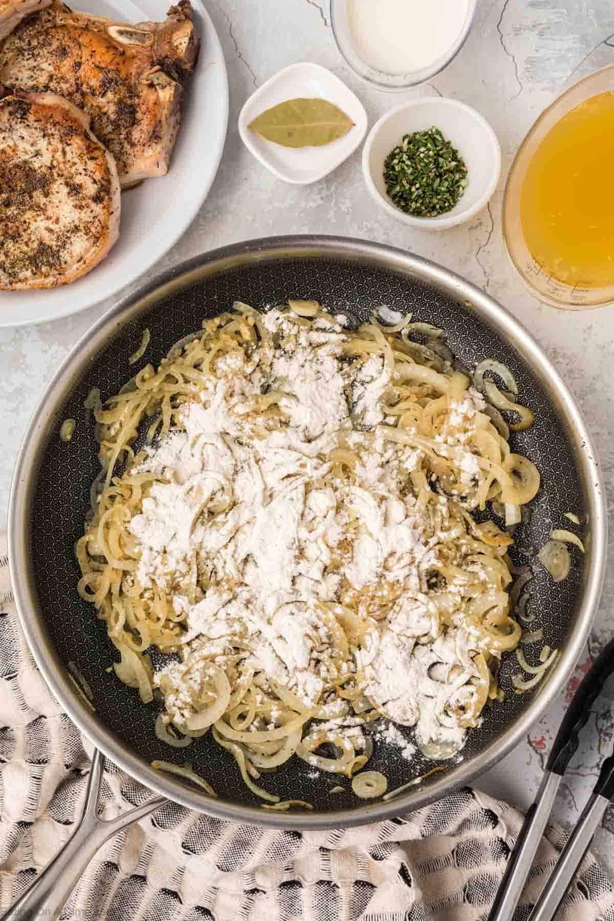 Flour sprinkled on the top of caramelized onions in a skillet