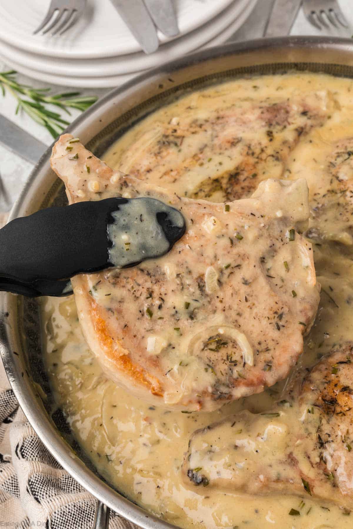 Smothered pork chops in a skillet with tongs holding one of the pork chops