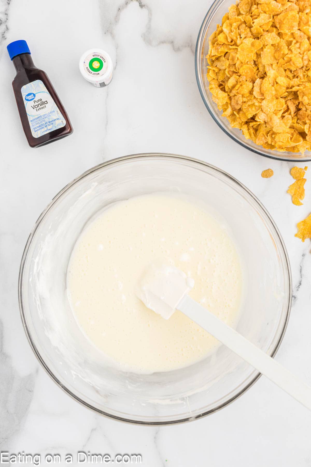 Melted marshmallow in a bowl with spatula with vanilla extract and a bowl of corn flakes on the side