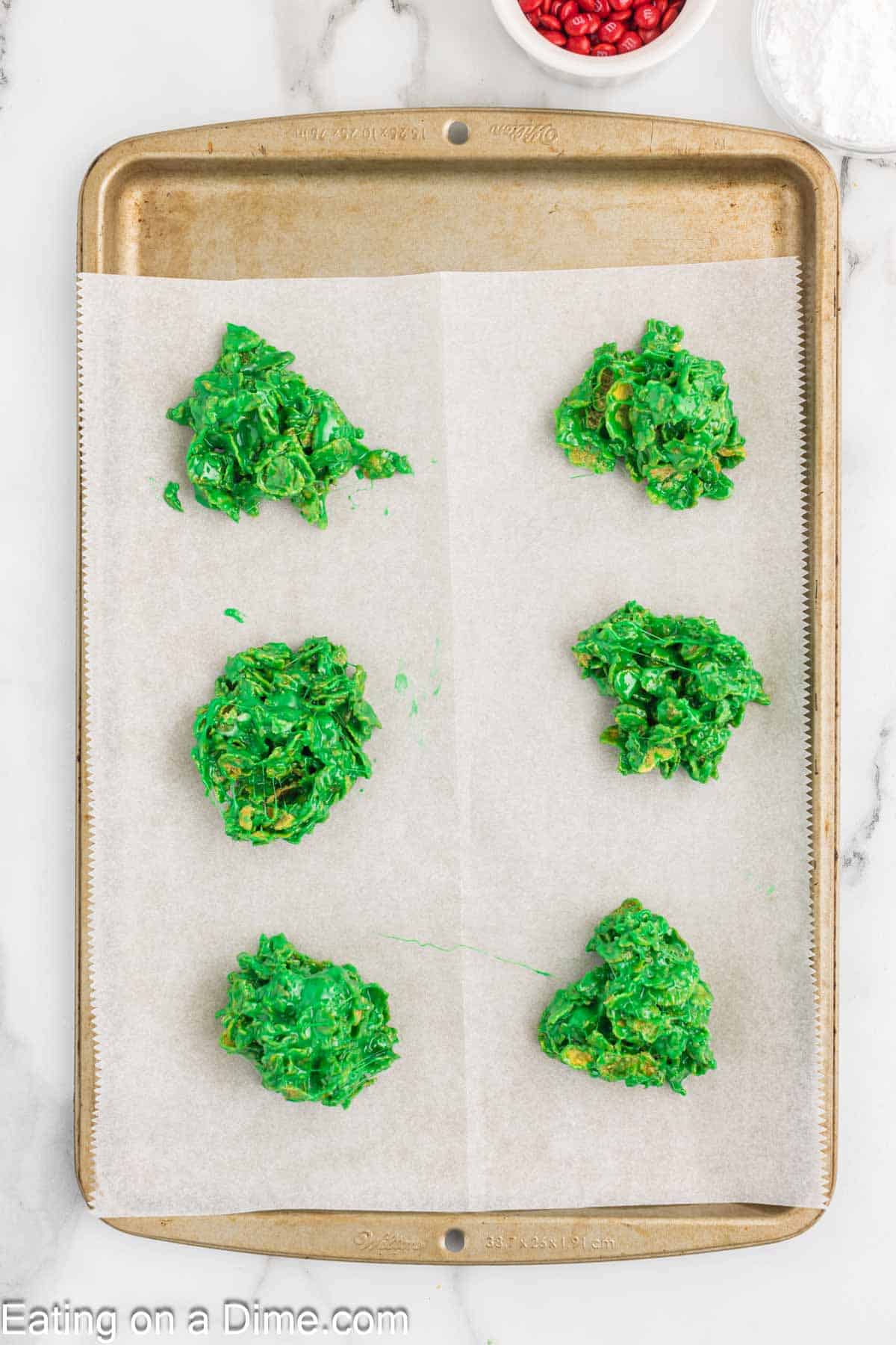 Green cereal mixture combined together in 6 piles on a baking sheet lined with parchment paper