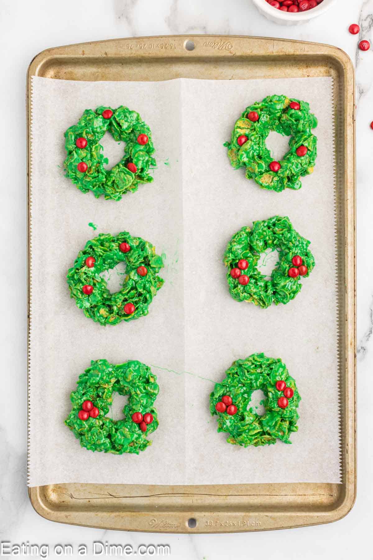 Christmas Wreath Cookies topped with red candy on a baking sheet lined with parchment paper