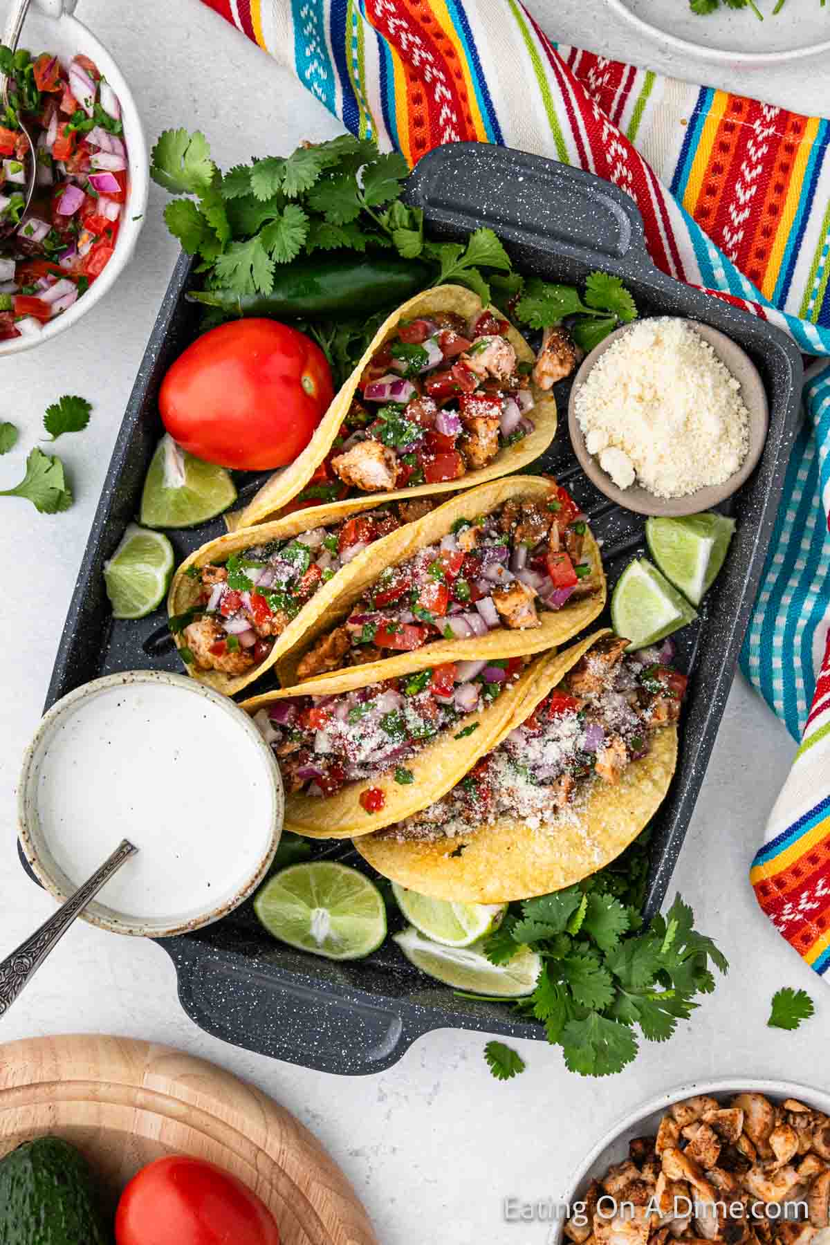 Chicken Street Tacos with corn tortillas on a platter with a bowl of grated cheese and a white sauce in a bowl. 