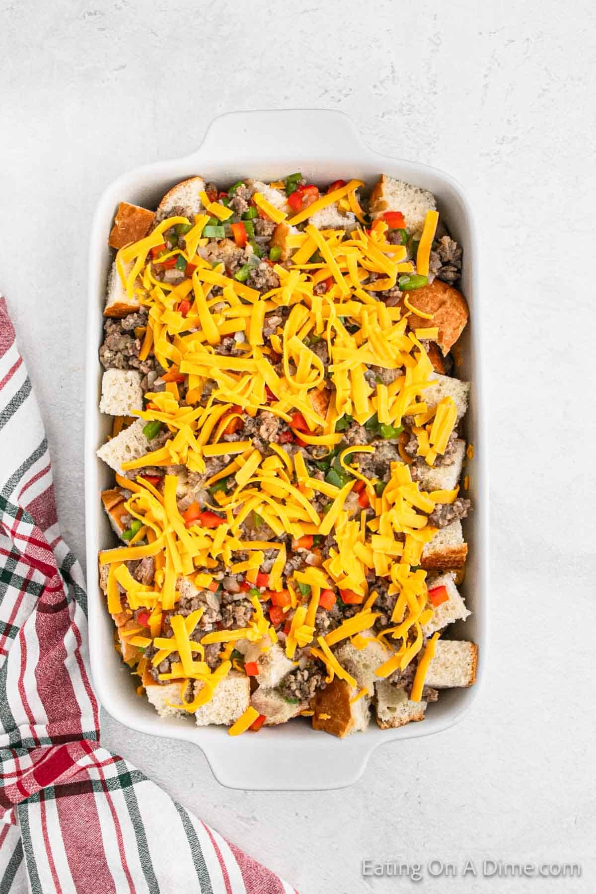 Shredded cheese topped with sausage, red and green bell peppers, and diced bread in a baking dish