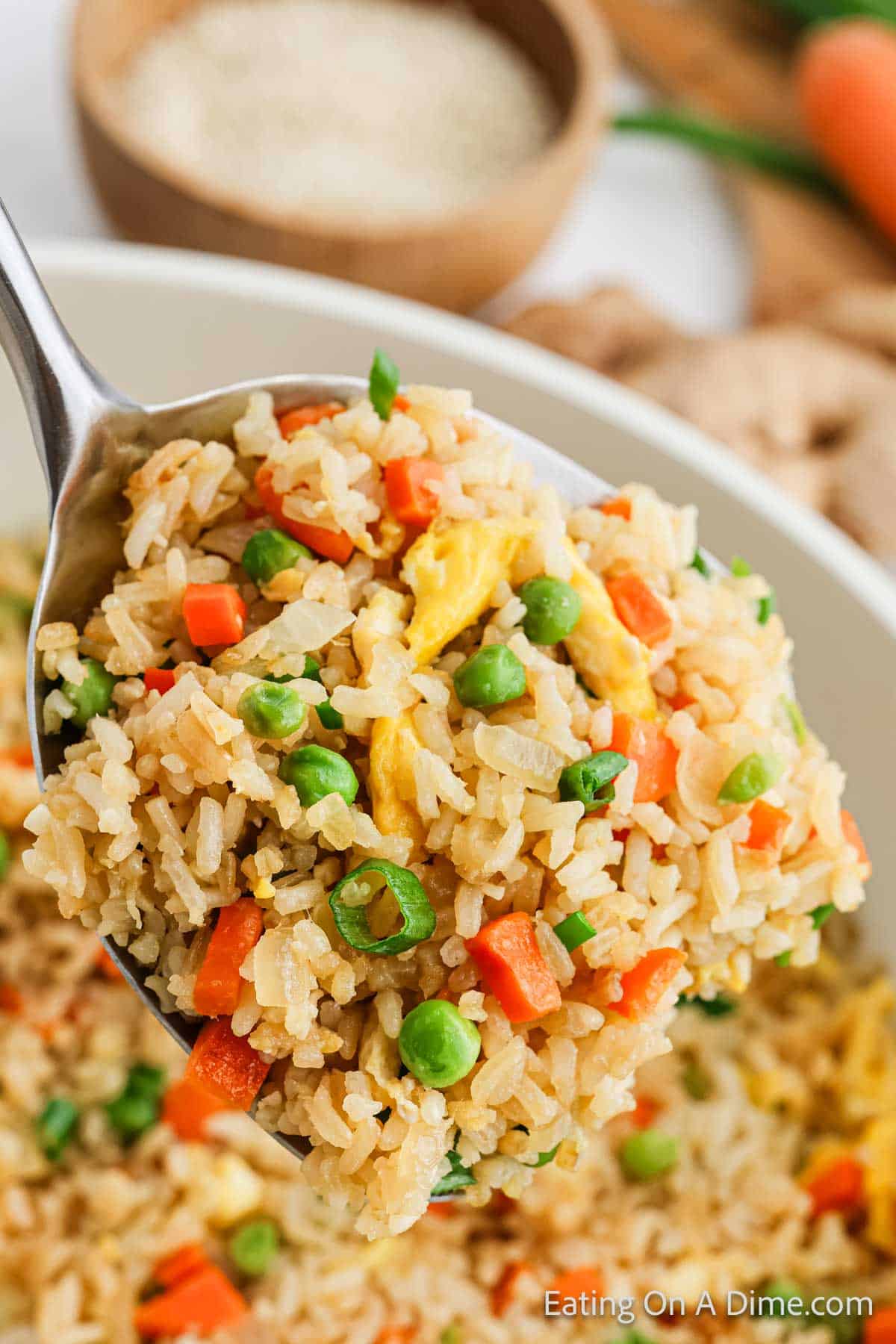 A spoonful of homemade hibachi fried rice with peas, carrots, and scrambled eggs hovers over a bowl filled with more deliciousness. In the background, a bowl of sesame seeds awaits its turn to elevate the flavor adventure.