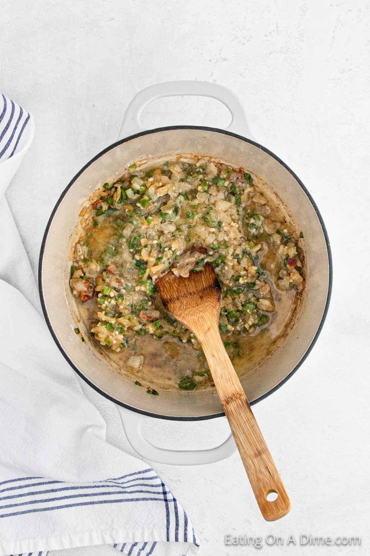 Adding broth to the cooked veggies mixture in a large pot with a wooden spoon