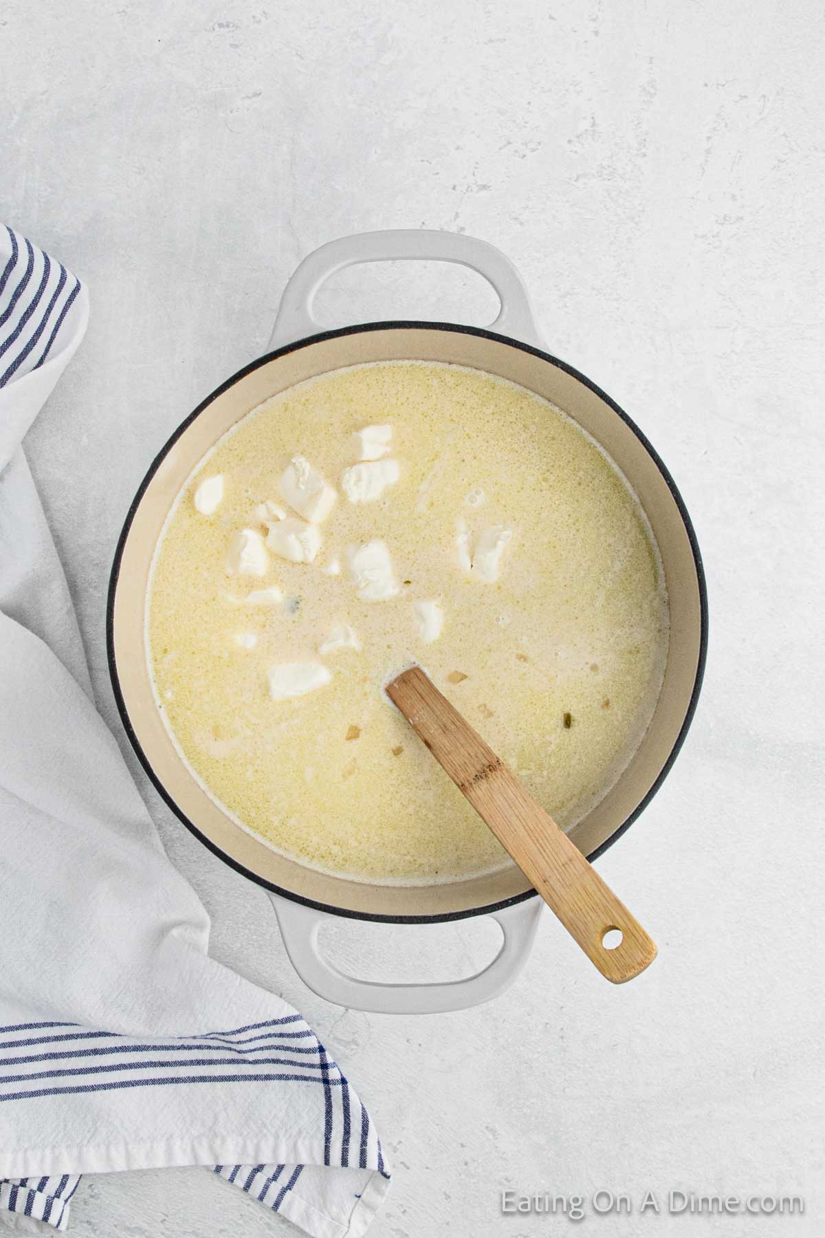 Diced cream cheese added to large pot with the soup mixture with a wooden spoon