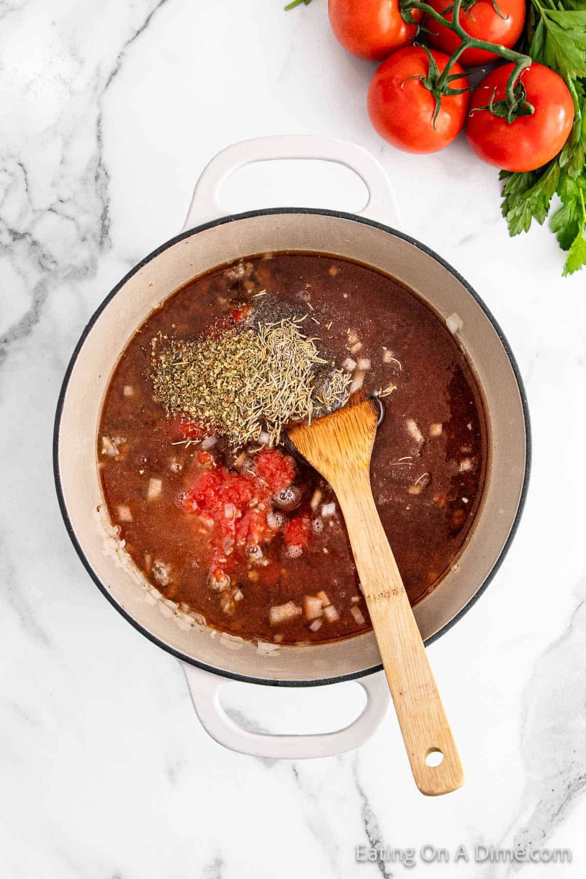 A pot of savory soup with diced tomatoes and herbs sits alongside a wooden spoon on a marble surface, reminiscent of lasagna flavors. Fresh tomatoes and parsley add vibrant color in the background.