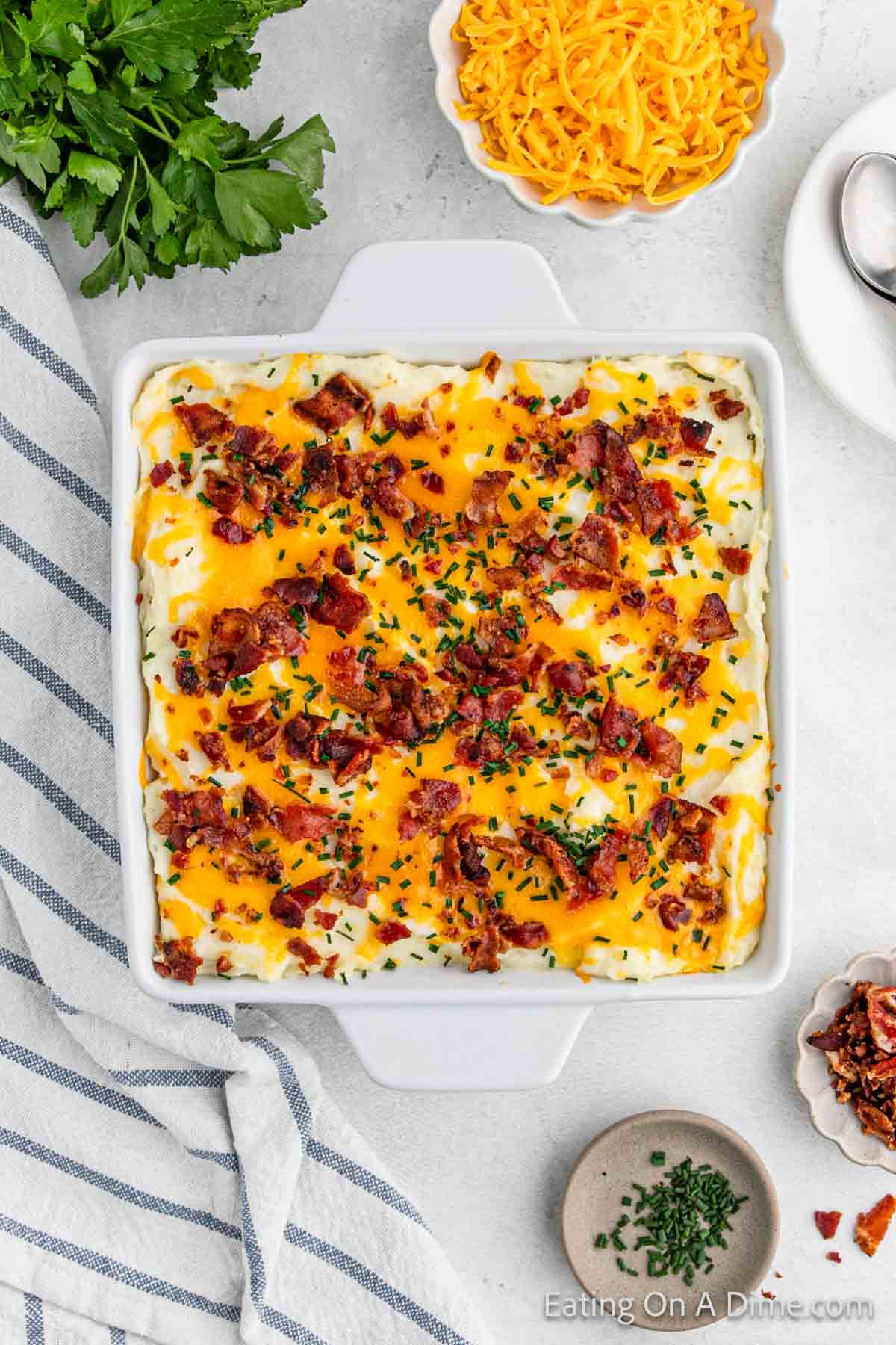 Mashed potato casserole in a baking dish topped with melted cheese, chopped bacon and chives