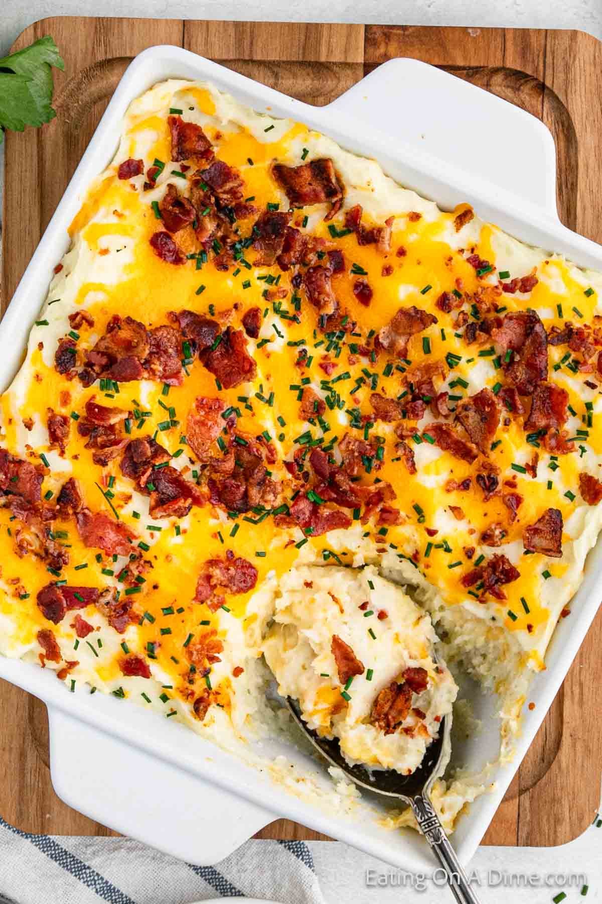 Mashed Potato Casserole in a baking dish topped with melted cheese, chopped bacon and chopped chives