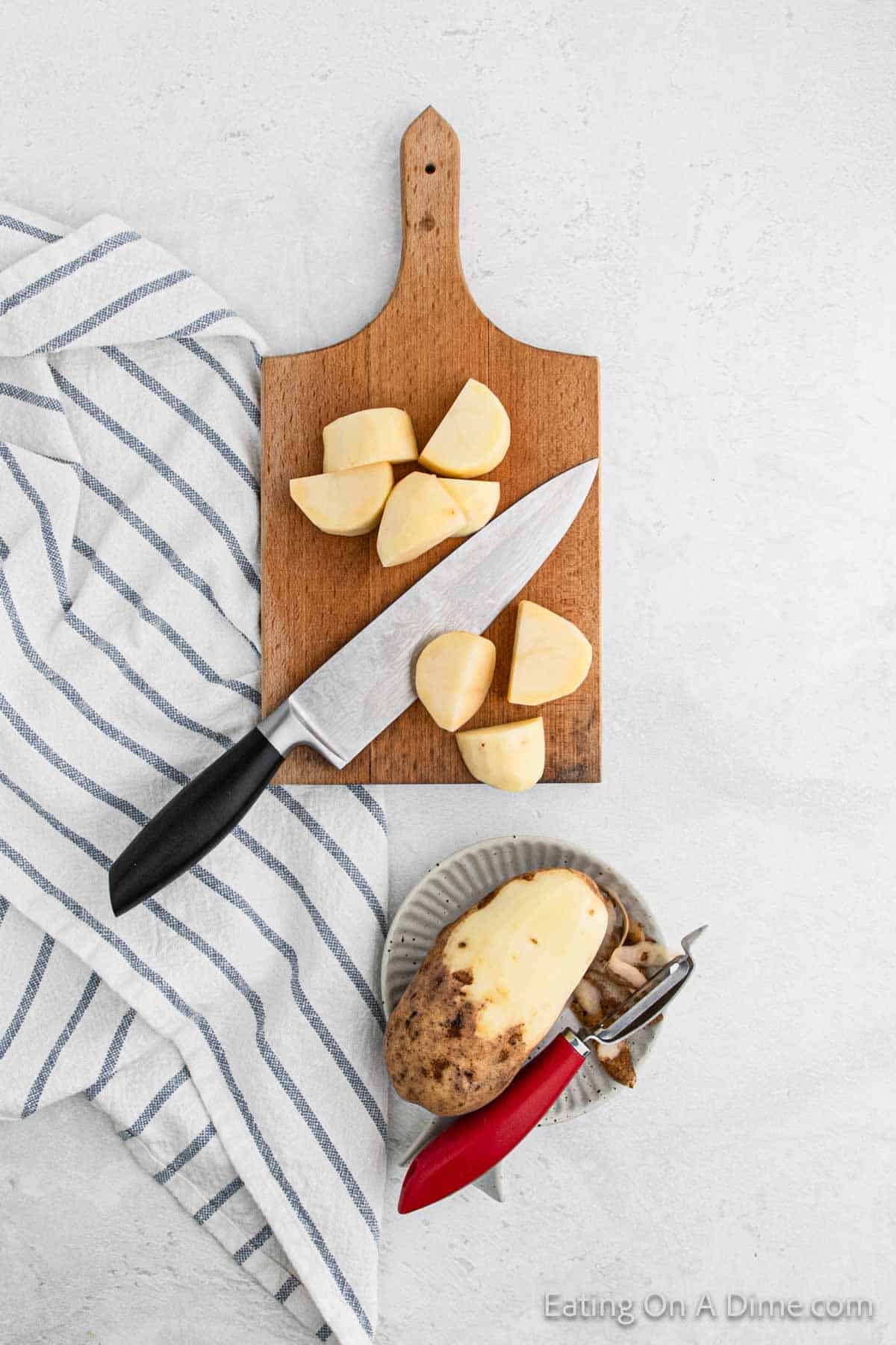 Dicing potatoes on a cutting board with a knife and half peeled potato