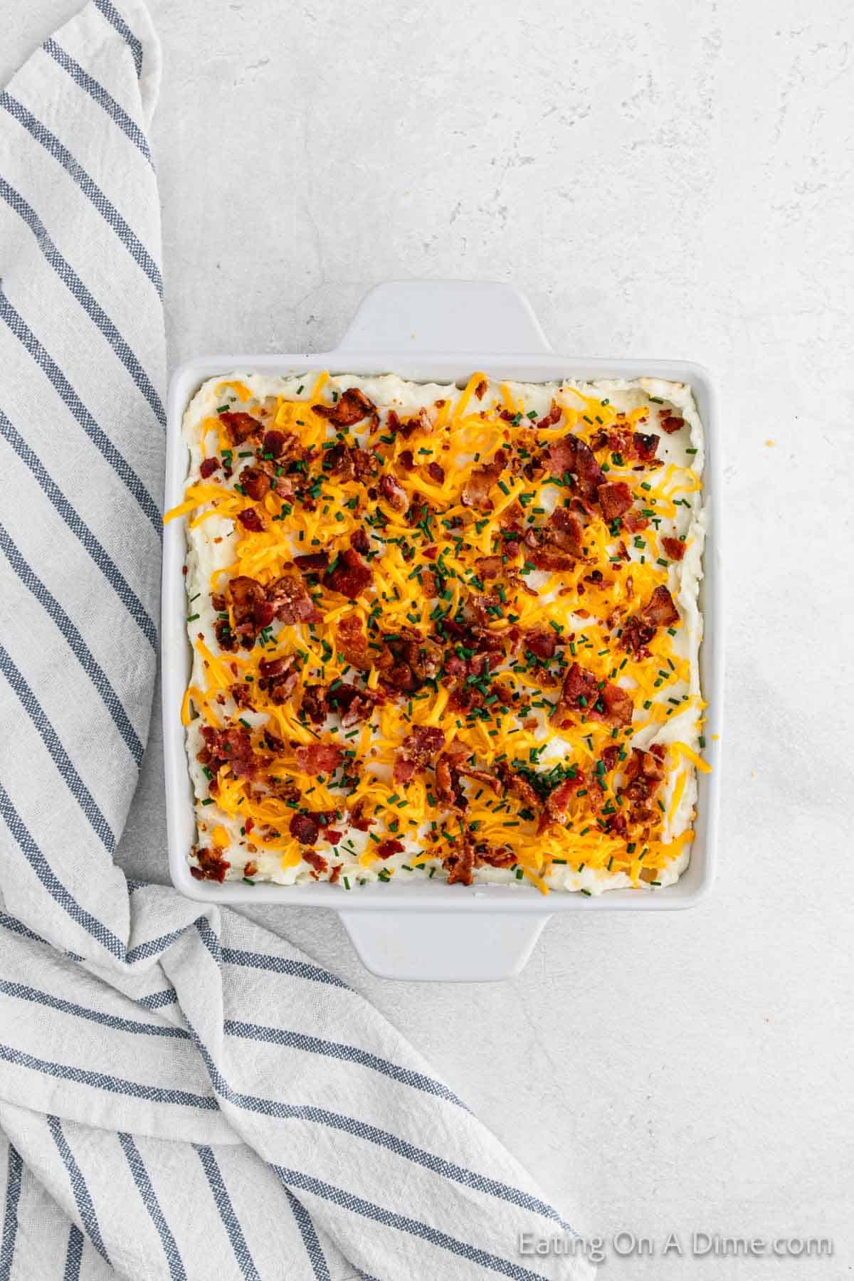 Topping mashed potatoes with shredded cheese, chopped bacon and chives