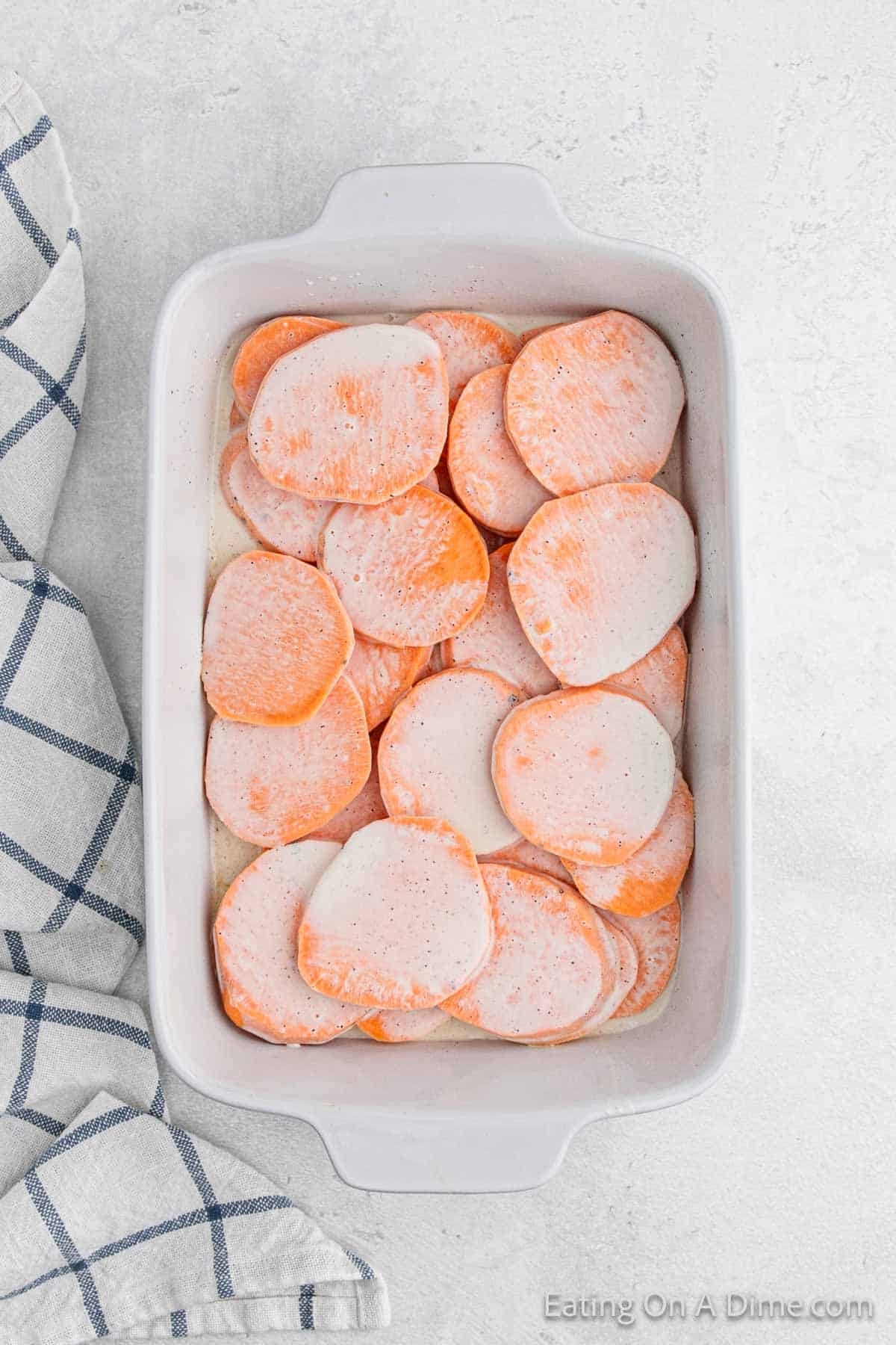 Pouring the sauce over the slice sweet potatoes in the baking dish