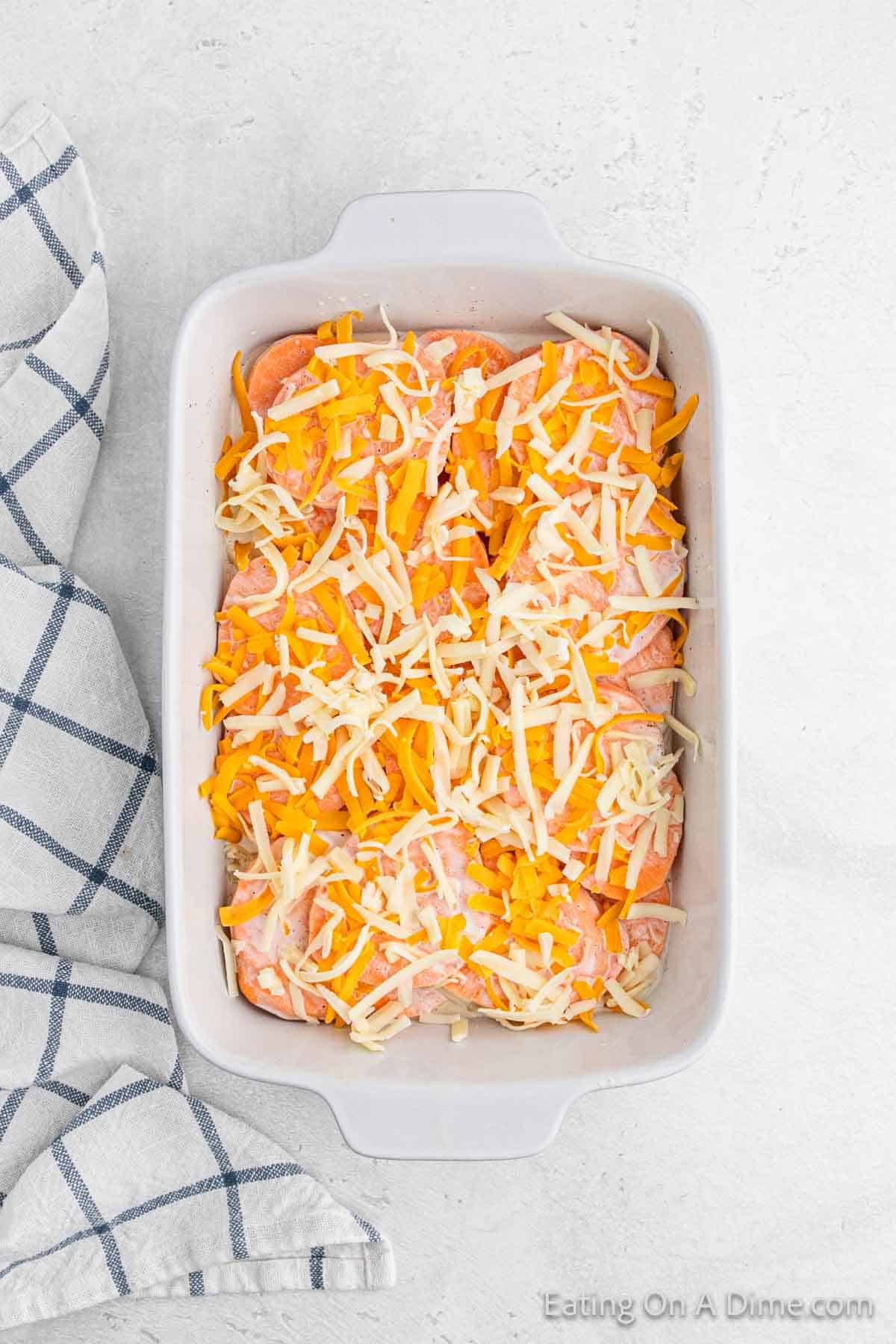 Topping the slice sweet potatoes with shredded cheese in a baking dish