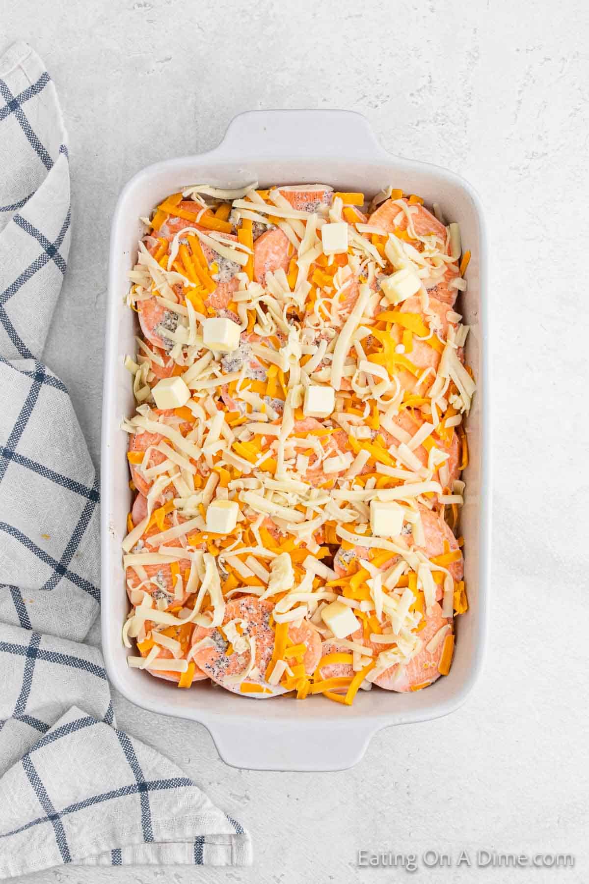 Slice sweet potatoes in a baking dish topped with shredded cheese and pieces of butter