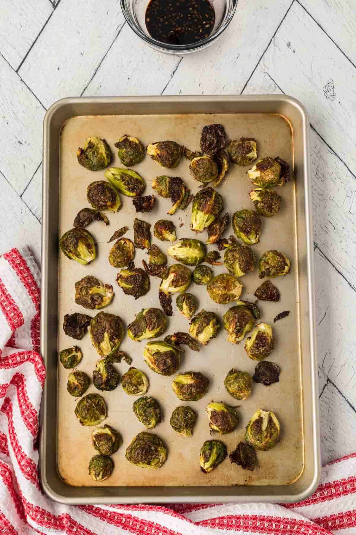 Roasted Brussel Sprouts on a baking sheet with a bowl of balsamic glaze on the side