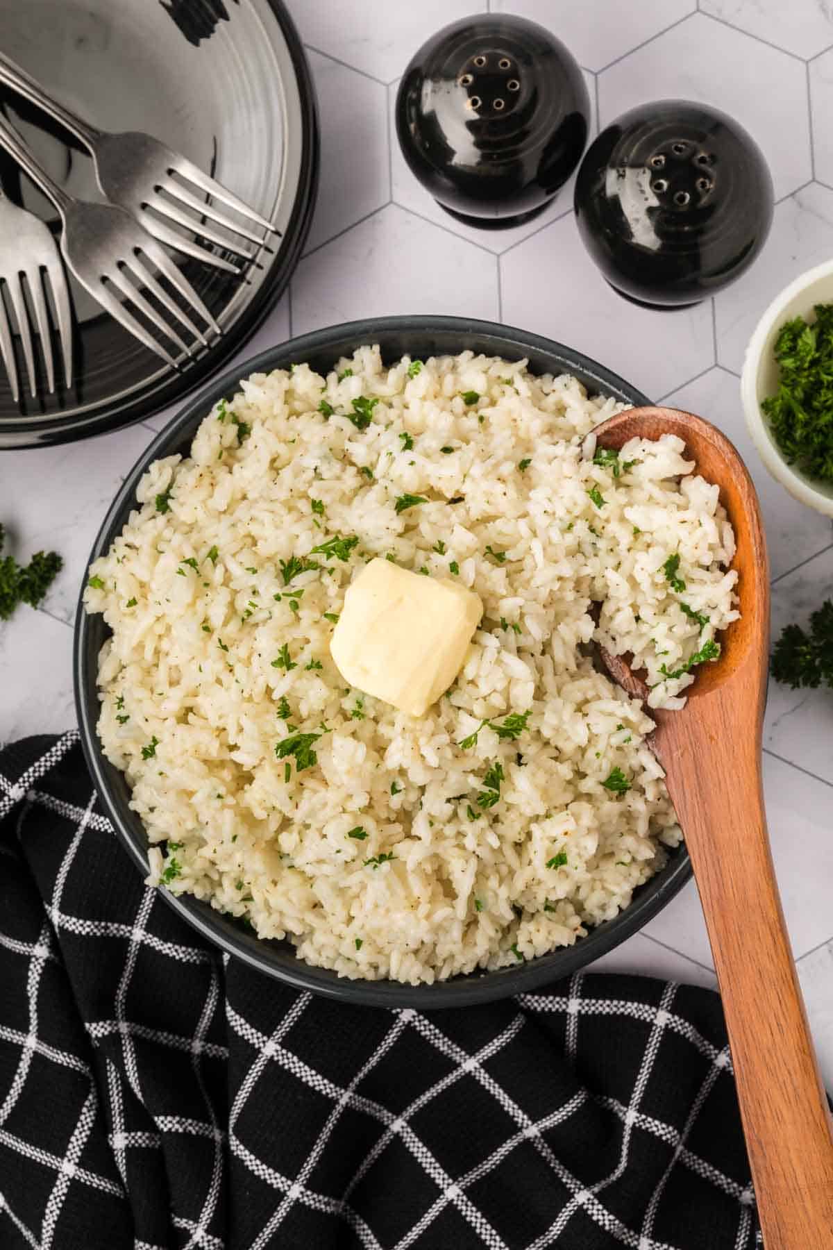 White rice topped with parsley and butter in a bowl with a wooden spoon