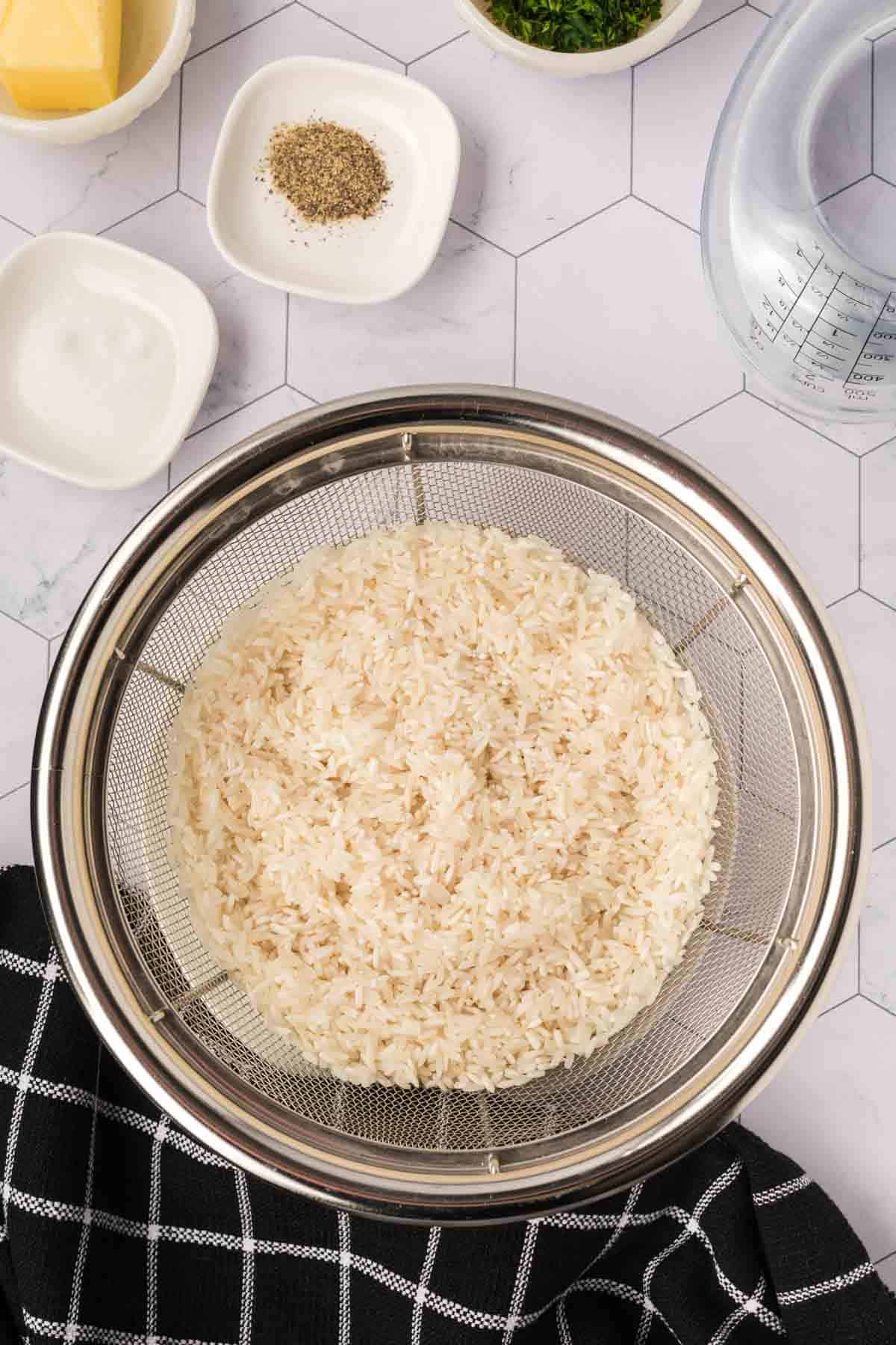 White rice in a colander with small bowls of salt, pepper and parsley