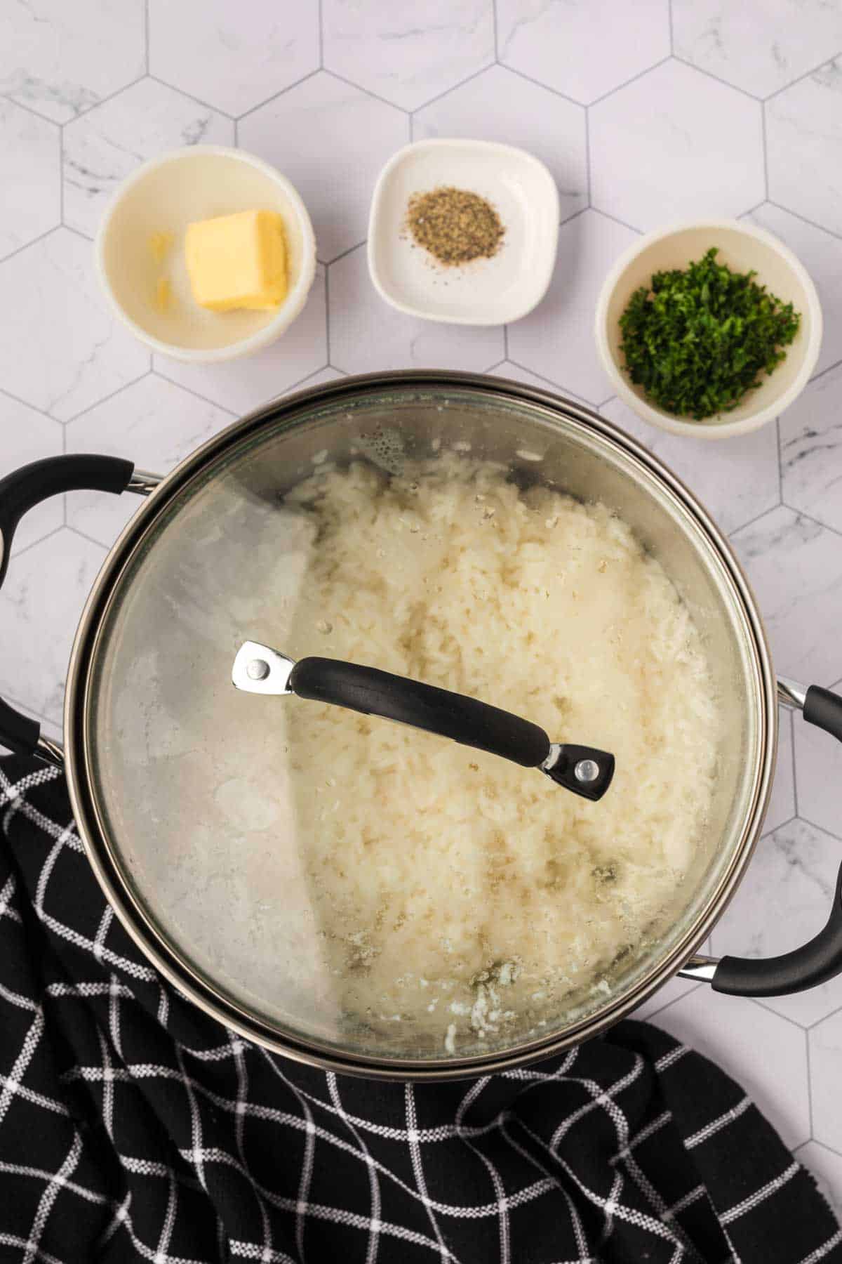 Large pot of rice covered with a lid with small bowl of butter, pepper, and parsley