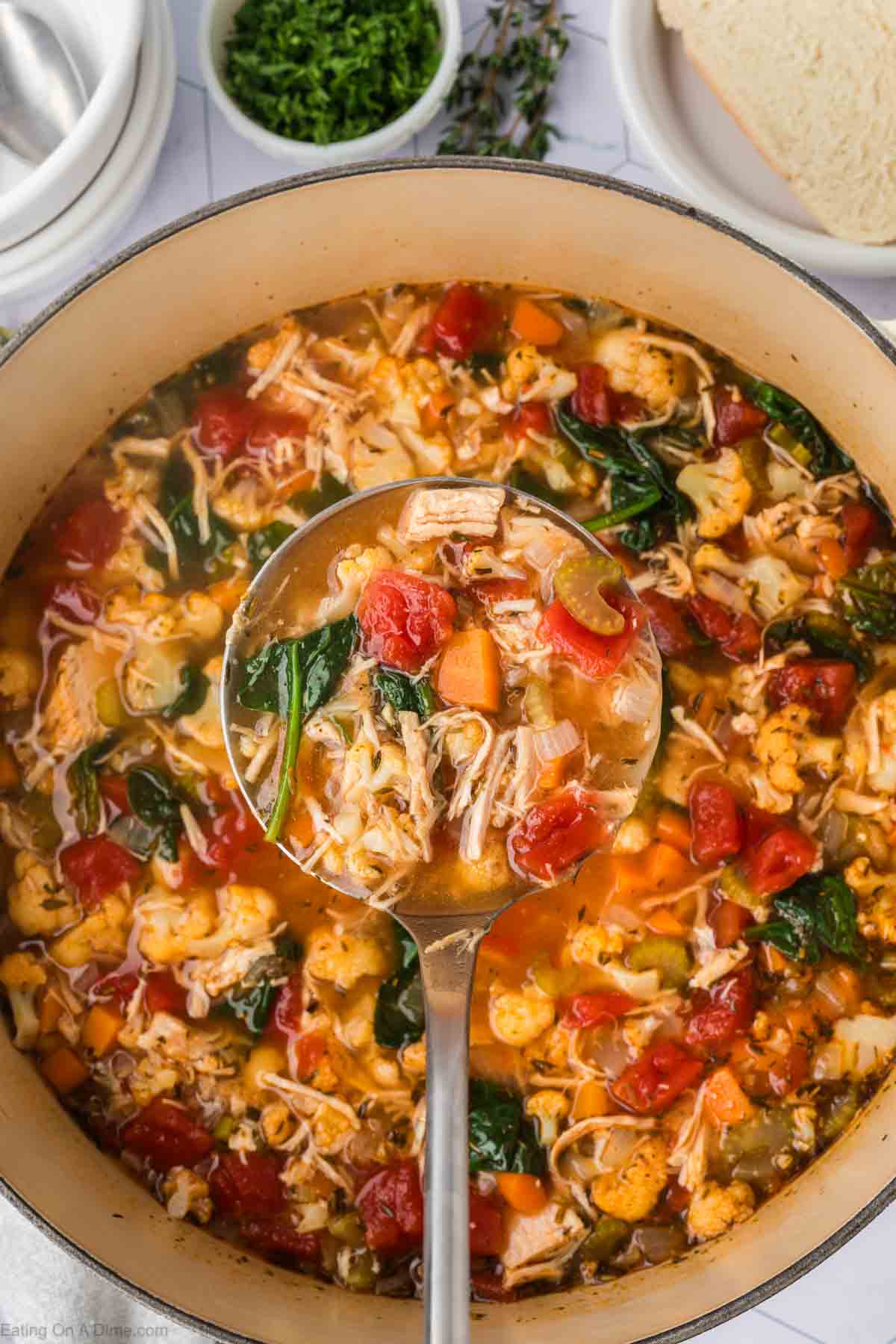 Turkey Soup with vegetables and cooked spinach in a large pot with a serving on a ladle