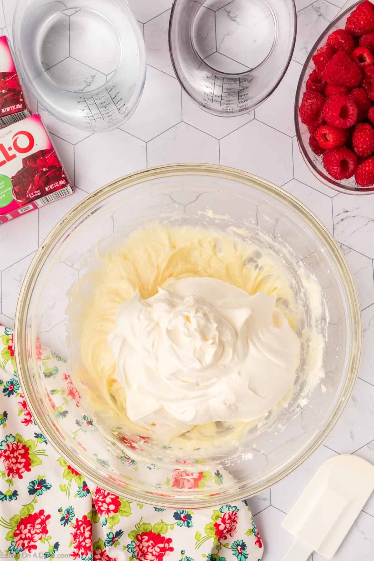 Cream cheese and powdered sugar mixed together topped with whipped cream in a bowl