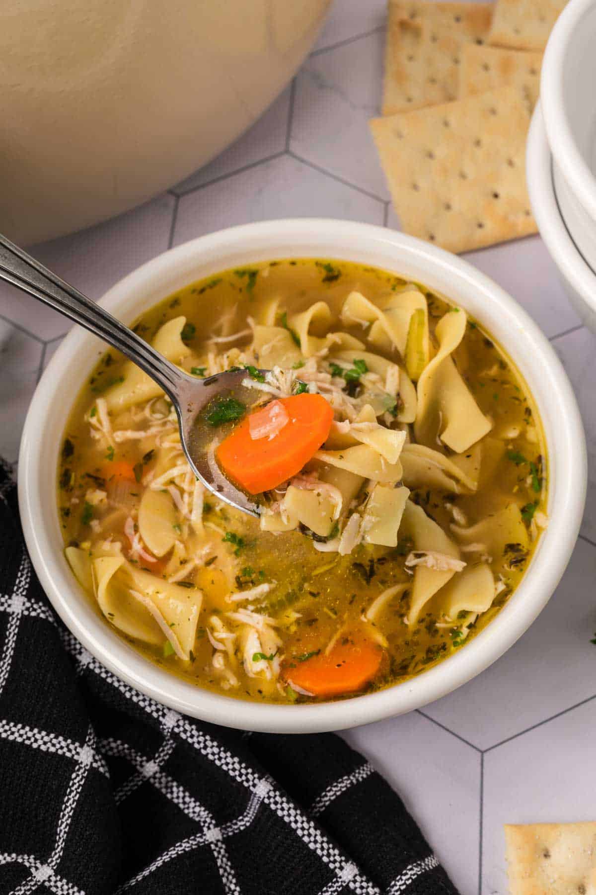 A bowl of turkey noodle soup with a bite on the spoon