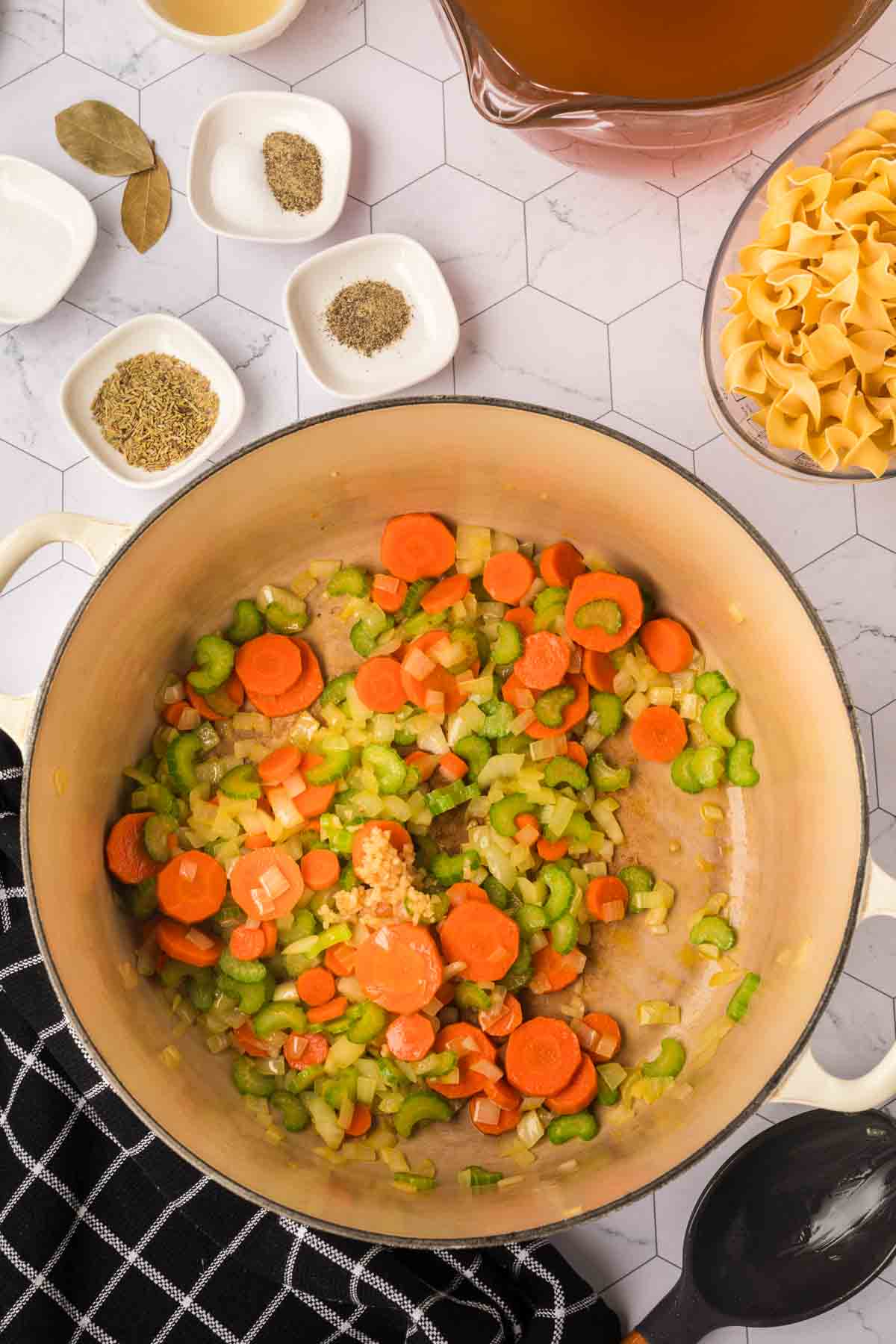 Cooked slice carrots, celery and onions in a large pot topped with minced garlic with small bowls of spices on the side