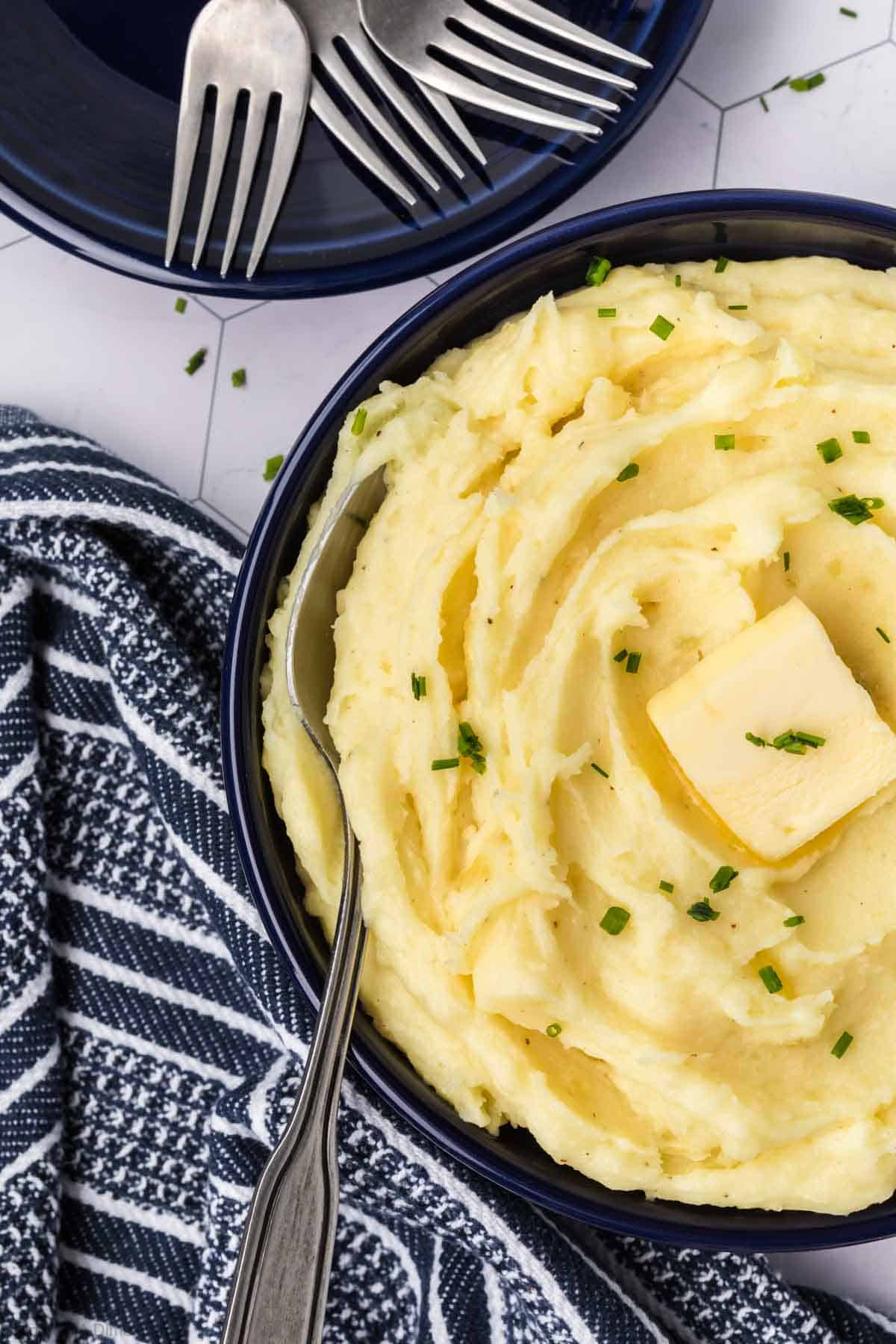 Yukon Gold Mashed Potatoes in a bowl topped with slice of butter and chives