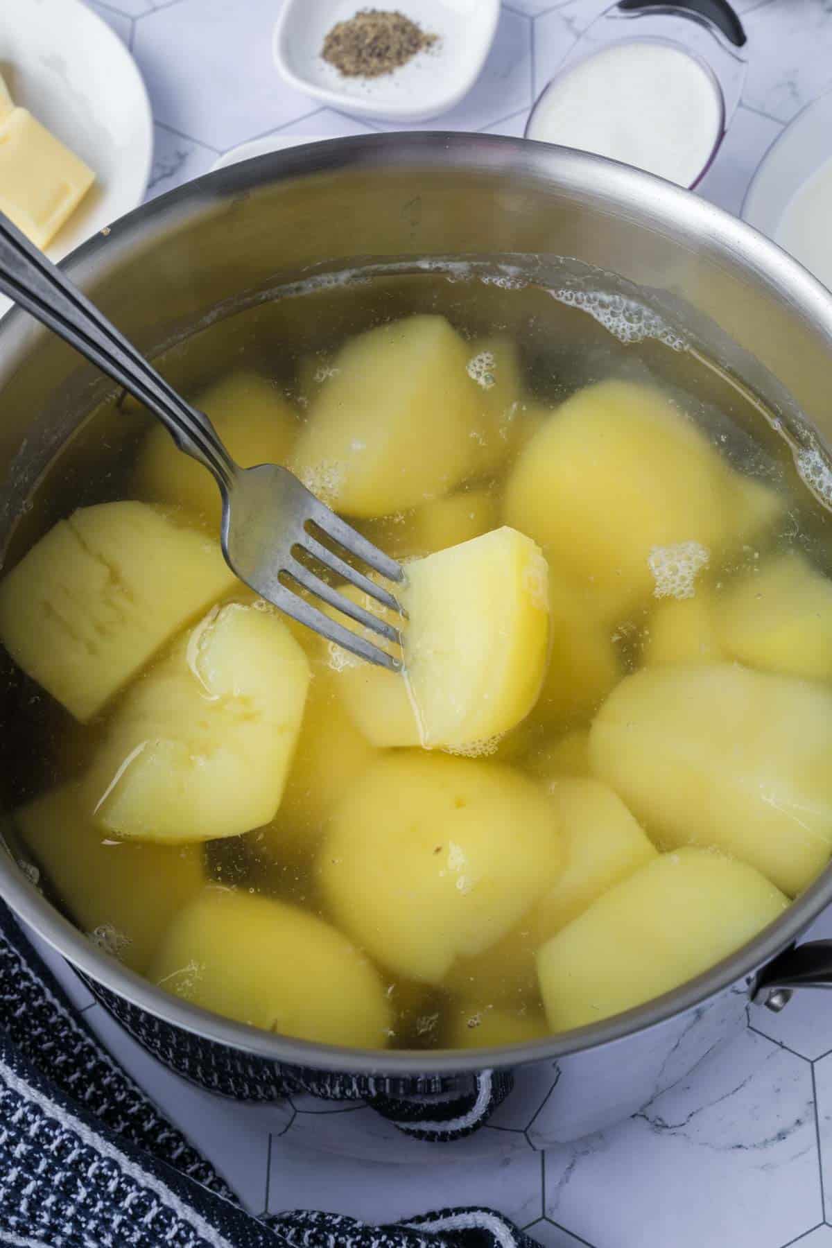 Diced potatoes in a large pot of water and a fork with potato on it