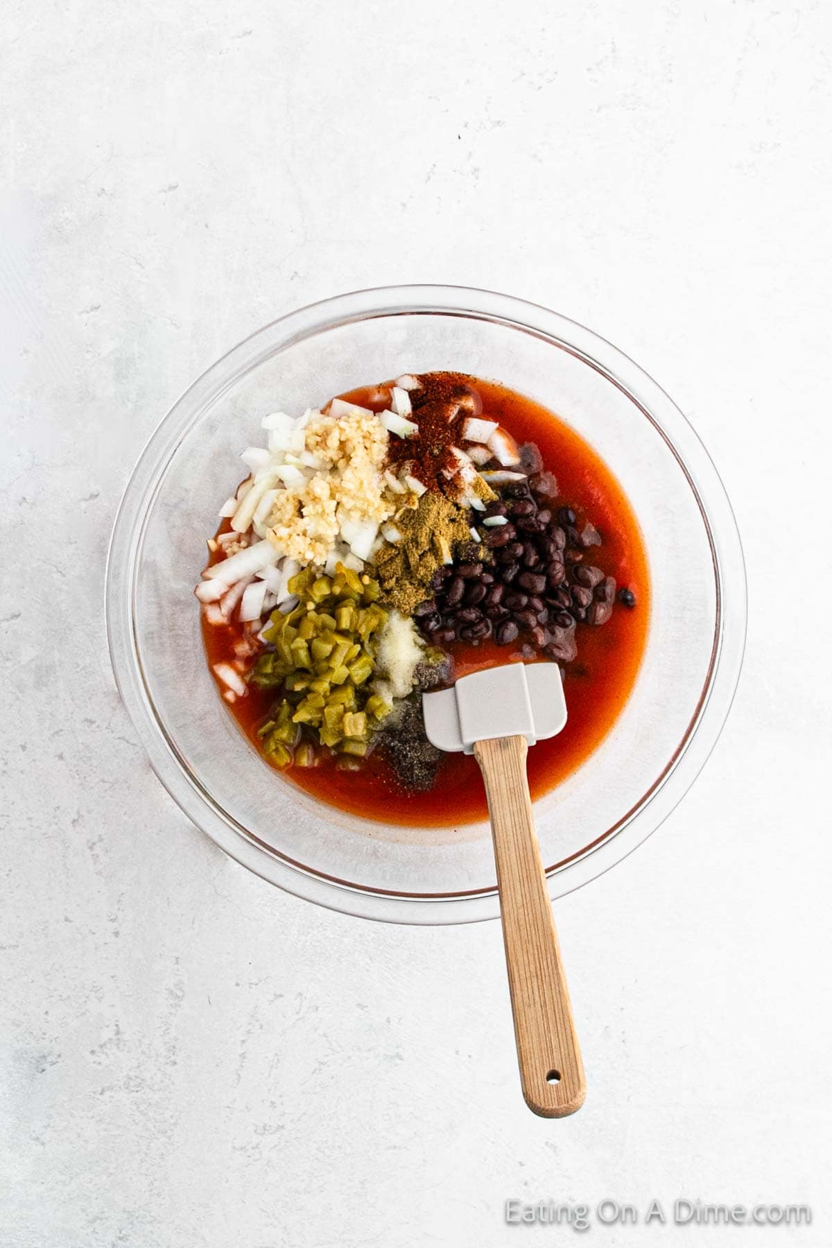 Combining the enchilada sauce, green chiles, black beans, chopped onions, and seasoning in a bowl with a spatula